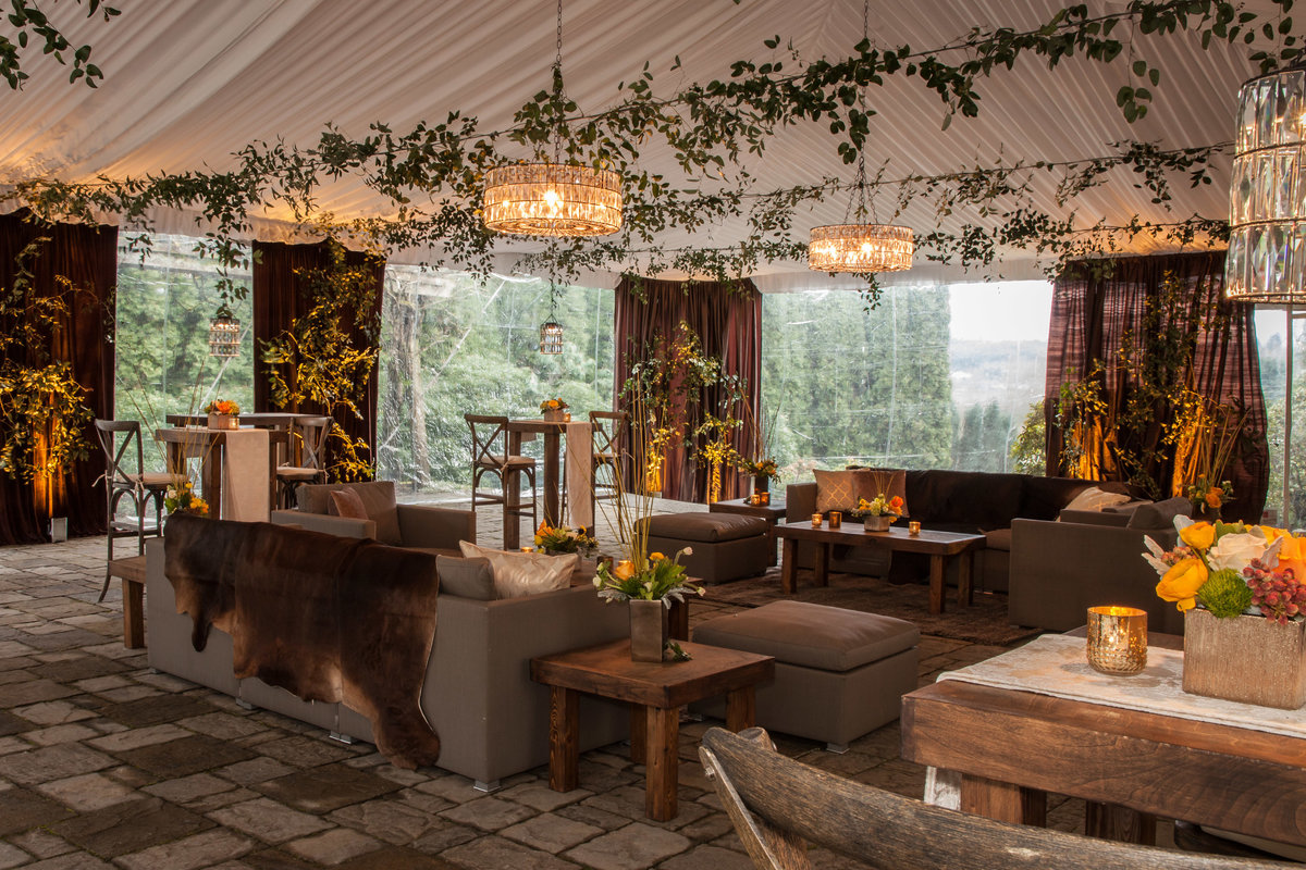 corporate party at Chateau Lill tent with ceiling greenery, lounge furniture, and yellow flowers, and brown draping, fur on sofa, gold candles