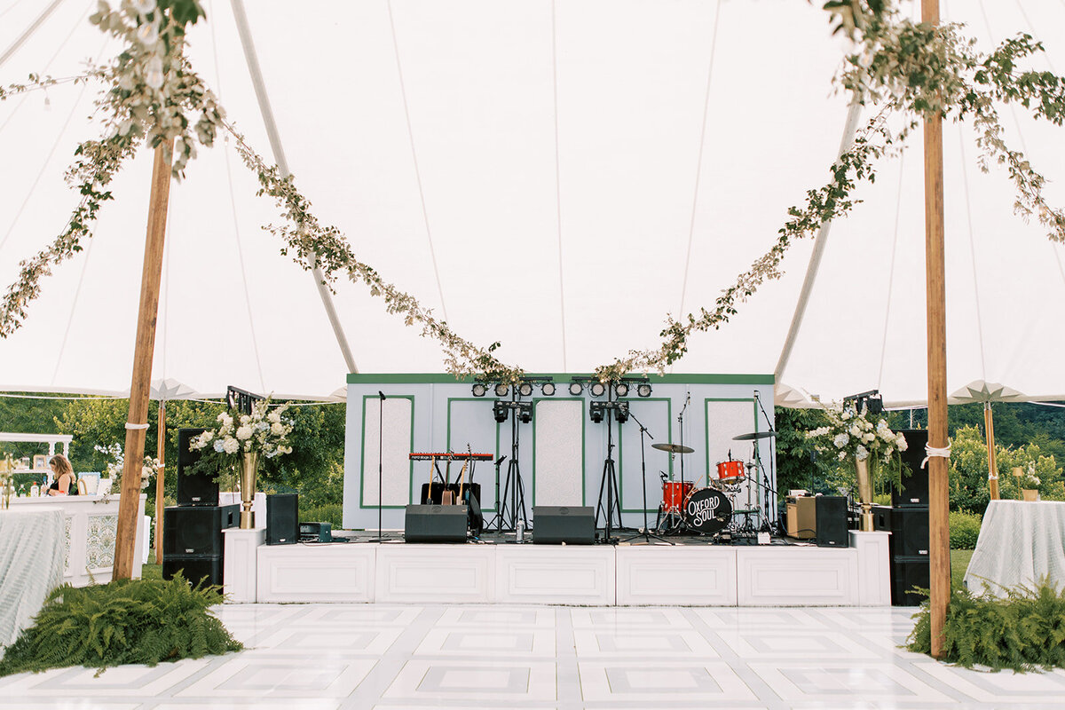  Sailcloth tent reception featuring a custom band stage with greenery and soft white florals.