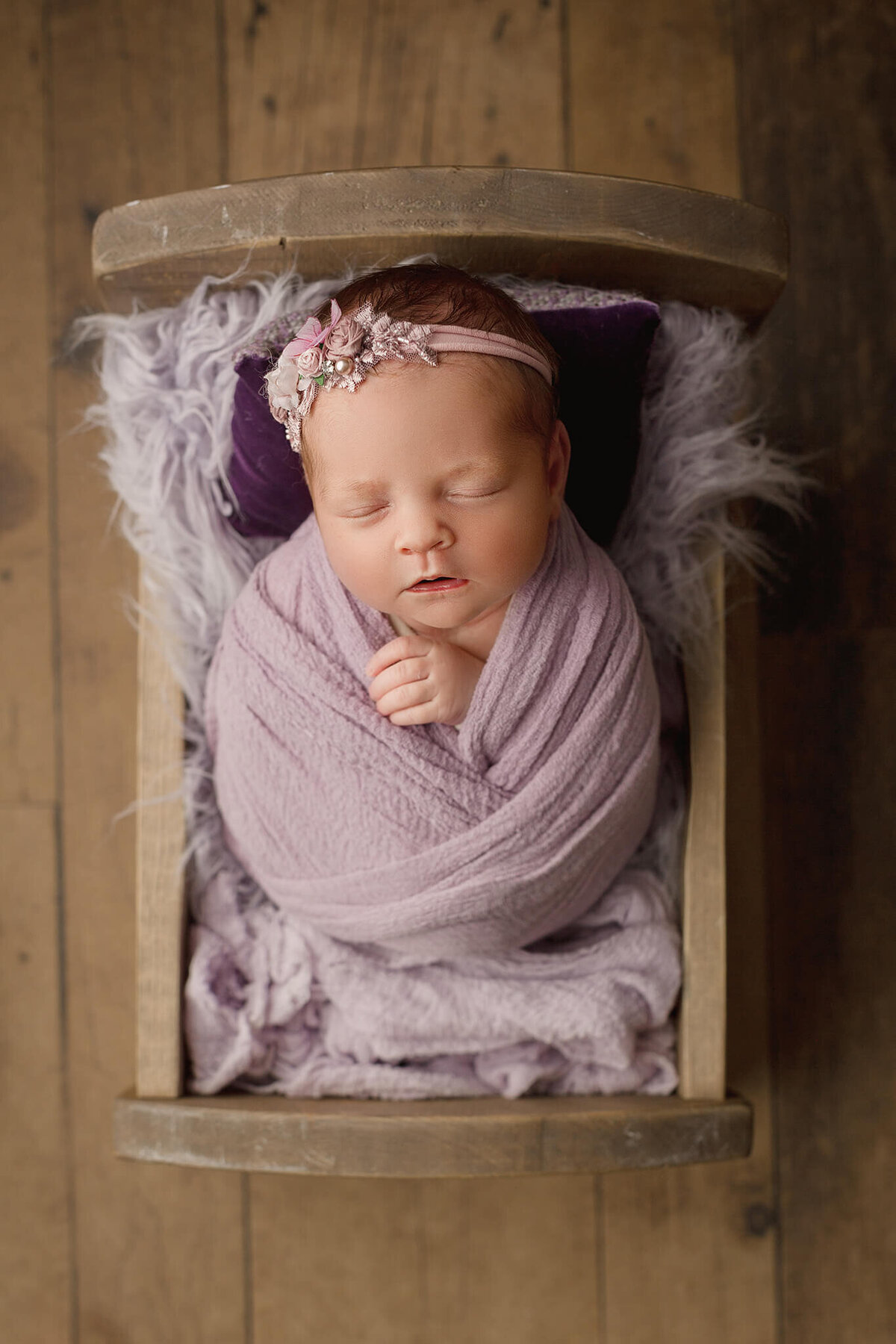 baby girl wrapped in purple, sleeping in wooden cradle