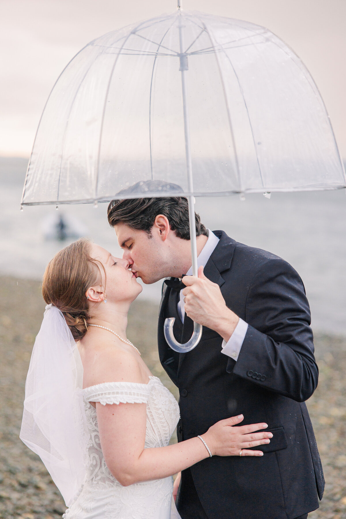 Bride and groom kissing underneath a clear umbrella representing candid Boston wedding photography
