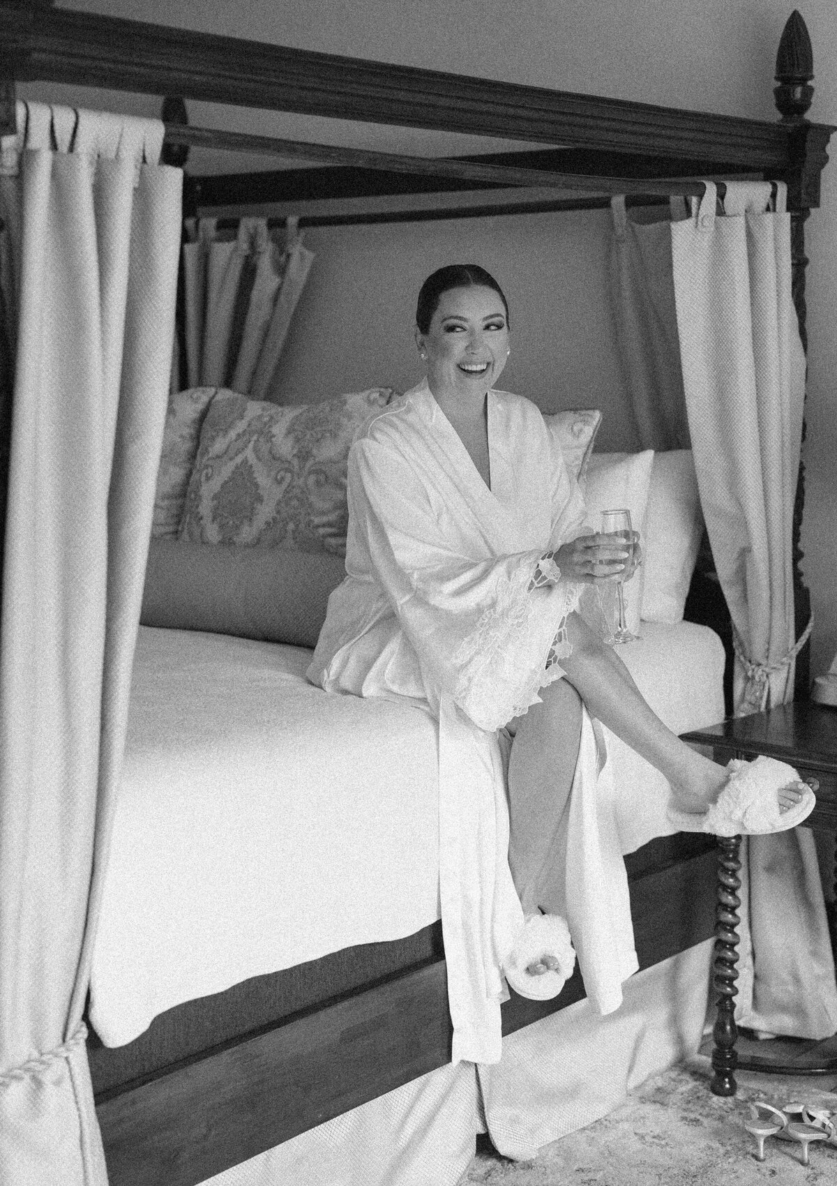 Bride in a white robe sitting on a canopy bed while getting ready for her fall wedding at Castle Ladyhawke.