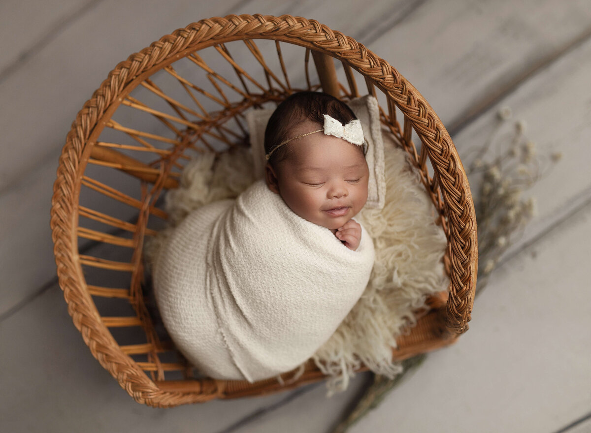 A newborn baby girl sleeps in a wicker chair on a pillow