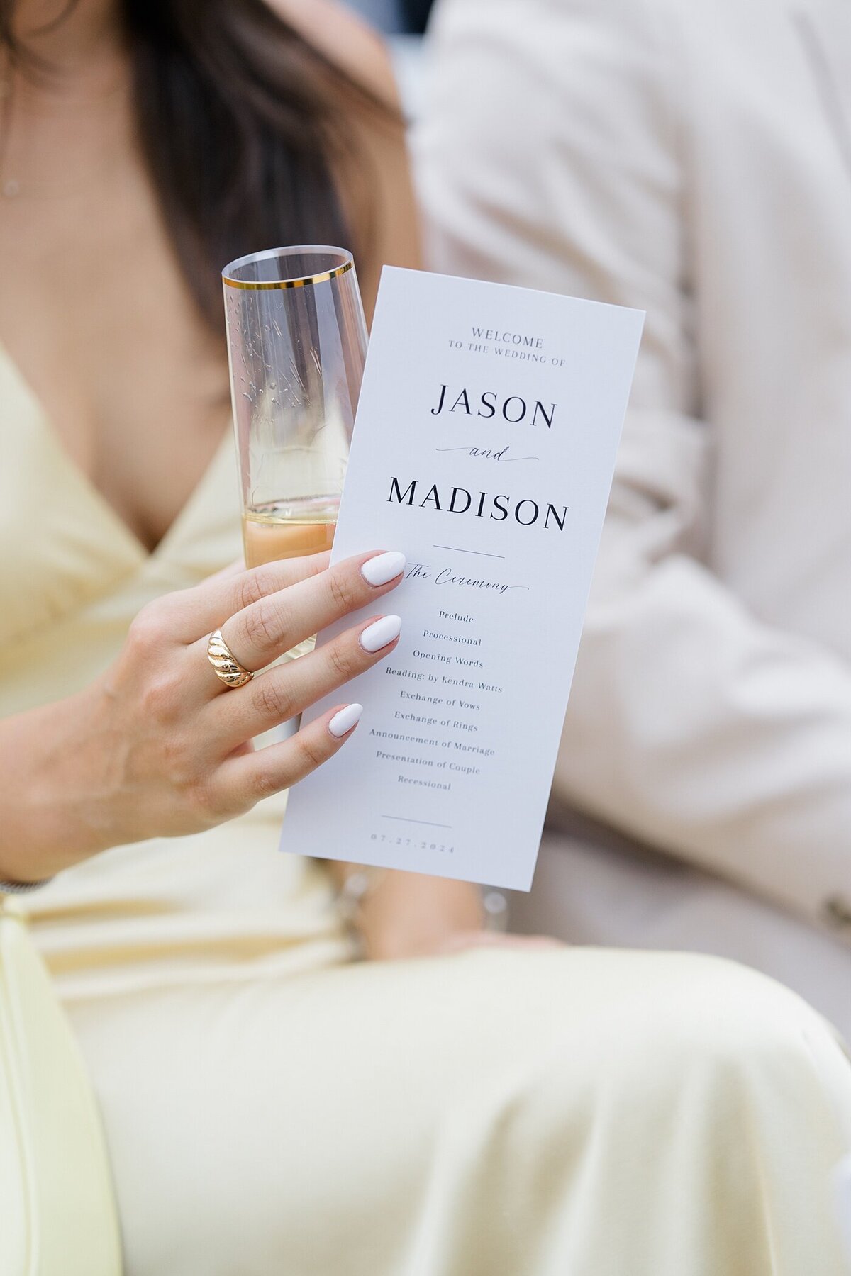 wedding guest in a light yellow dress holding a wedding day itinerary