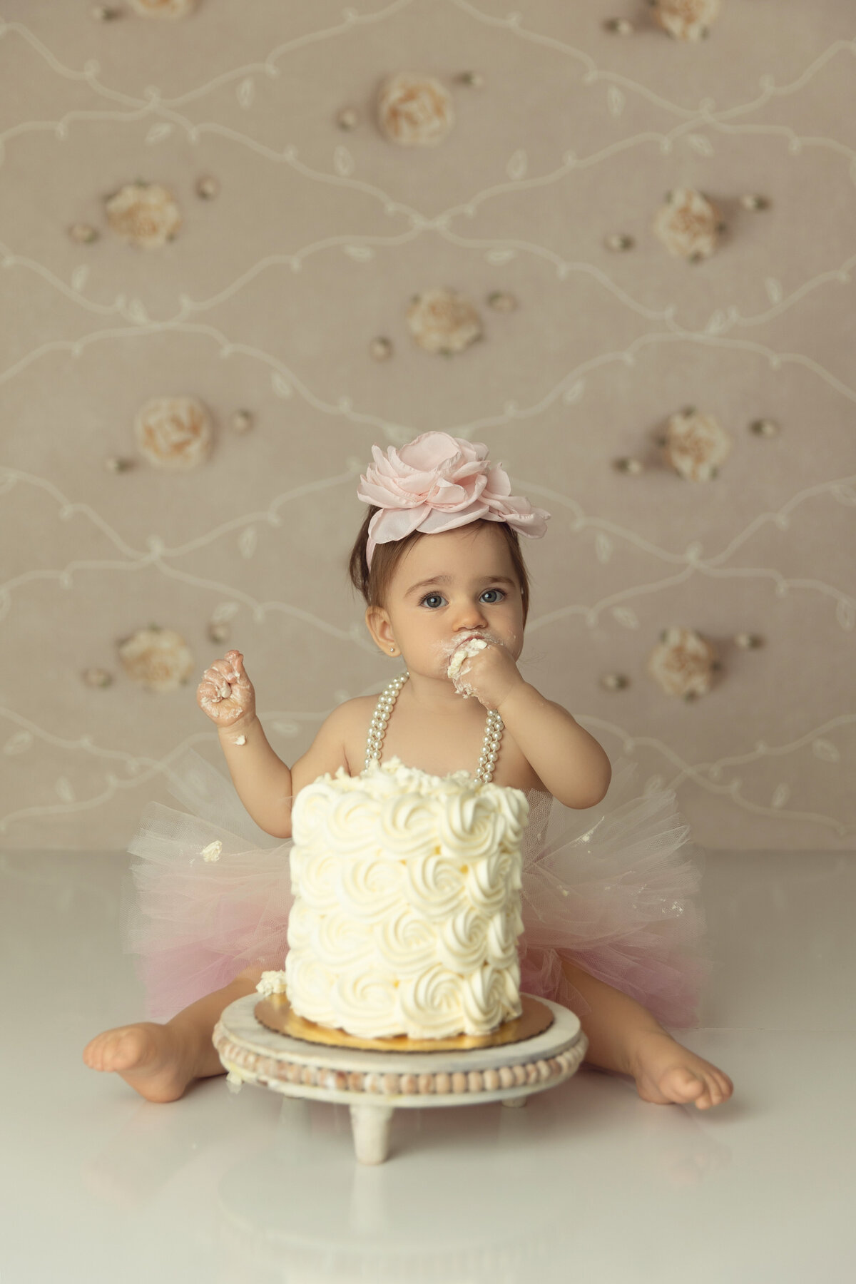 A toddler girl in a pink tutu shoves some cake in her mouth in a floral princess themed birthday photo session with a New Jersey Cake Smash Photographer