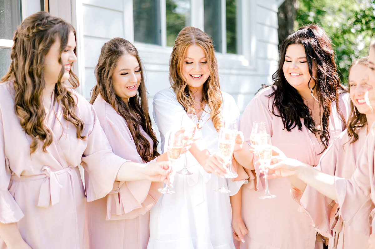 Niagara wedding photographer capturing bride and bridesmaids as they gather and cheers with champagne during getting ready pictures.