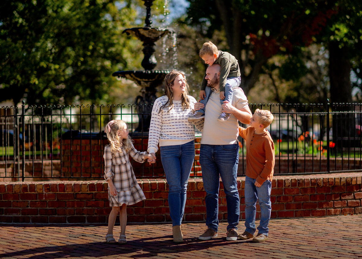 Mom Dad and their 3 kids look at each other and laugh in front of a fountain
