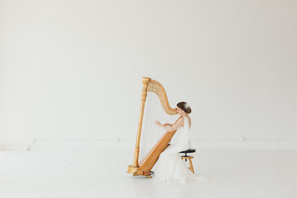woman in white gown is playing harp with all white surrounding her.