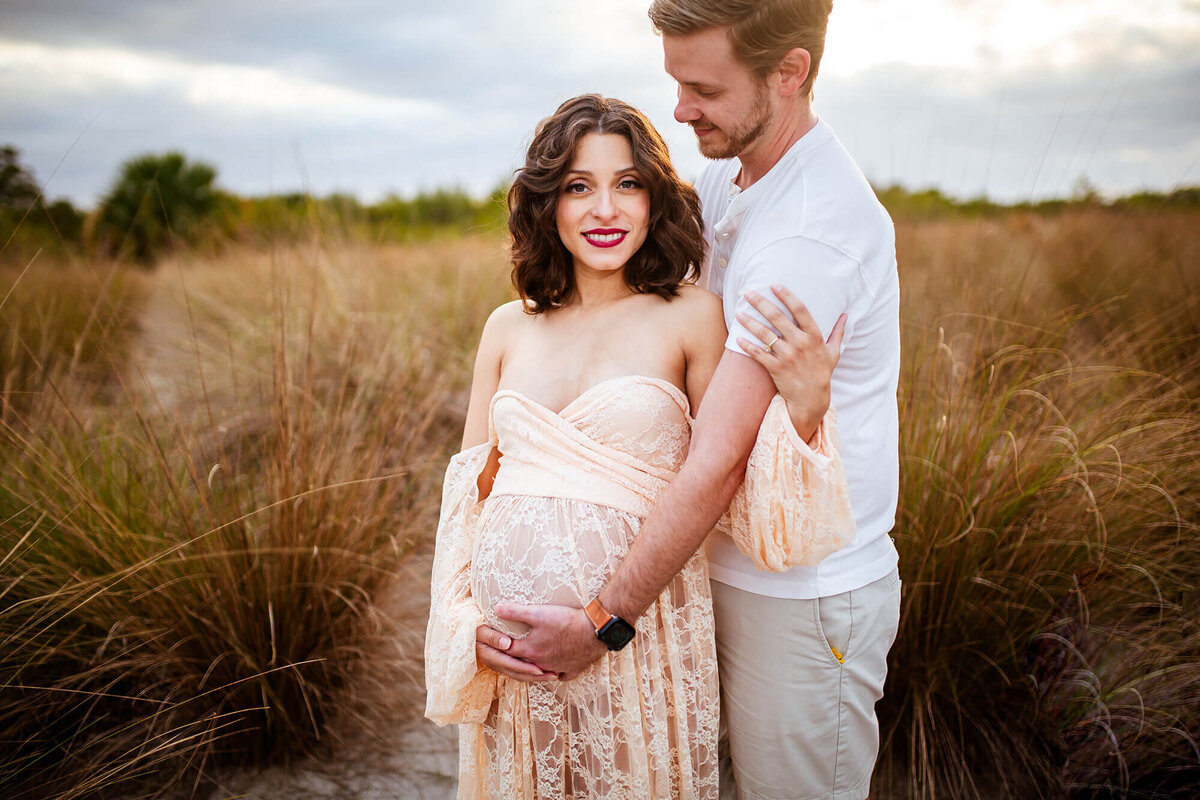 Husband looking lovingly at wife while holding wifes belly bump at Cypress Point park in Tampa, FL