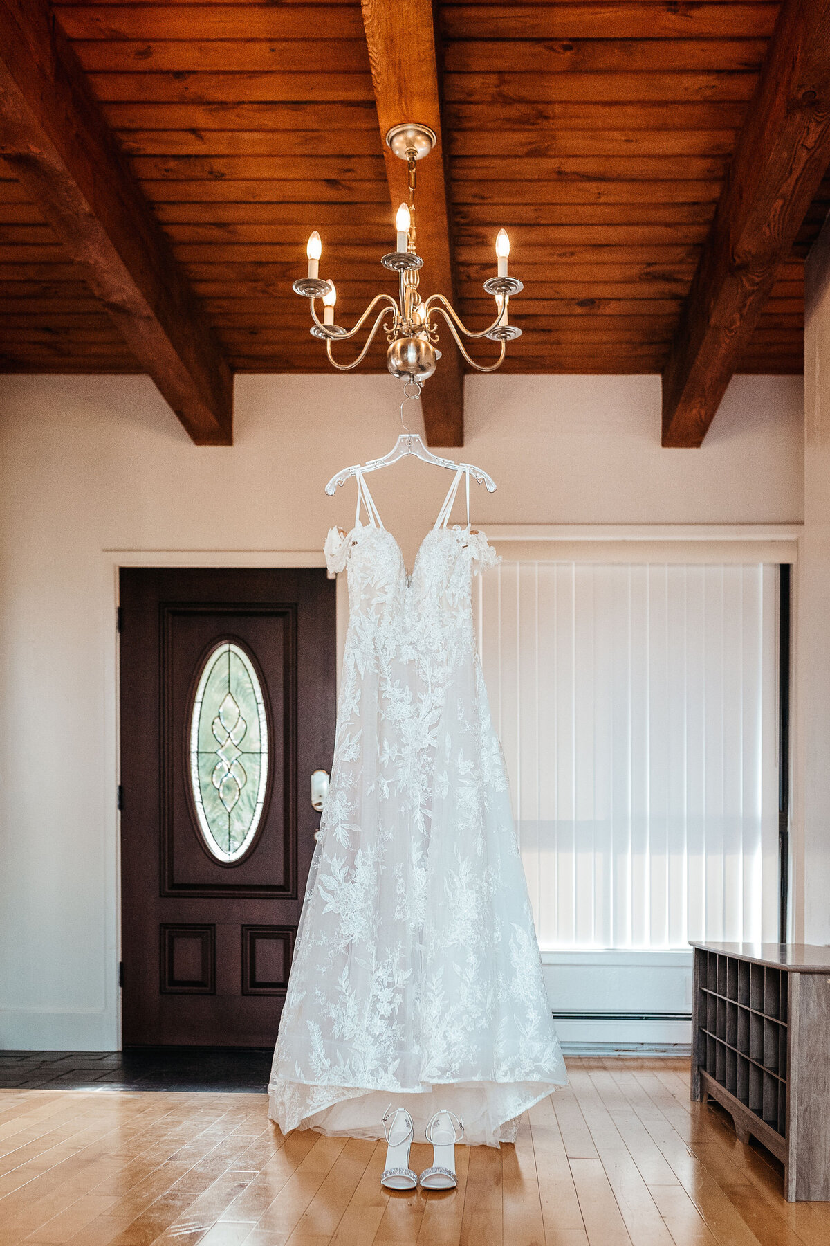 Wedding dress hanging from a chandelier in getting ready space at Sanborn Hill Farm wedding Venue by Lisa Smith Photography