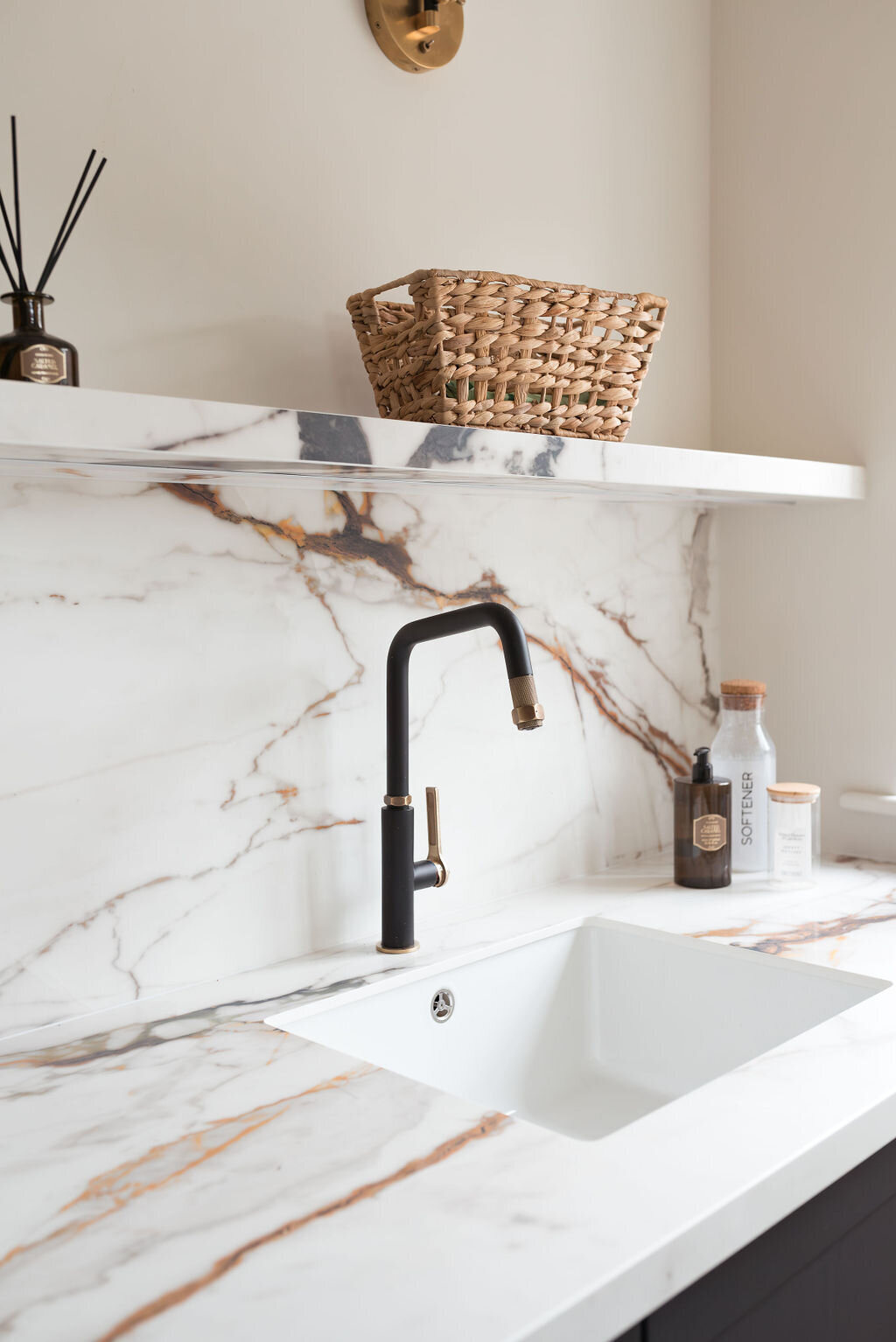 White marble countertop and backsplash veined with black and brown. A white farmhouse sink with modern black hardware.