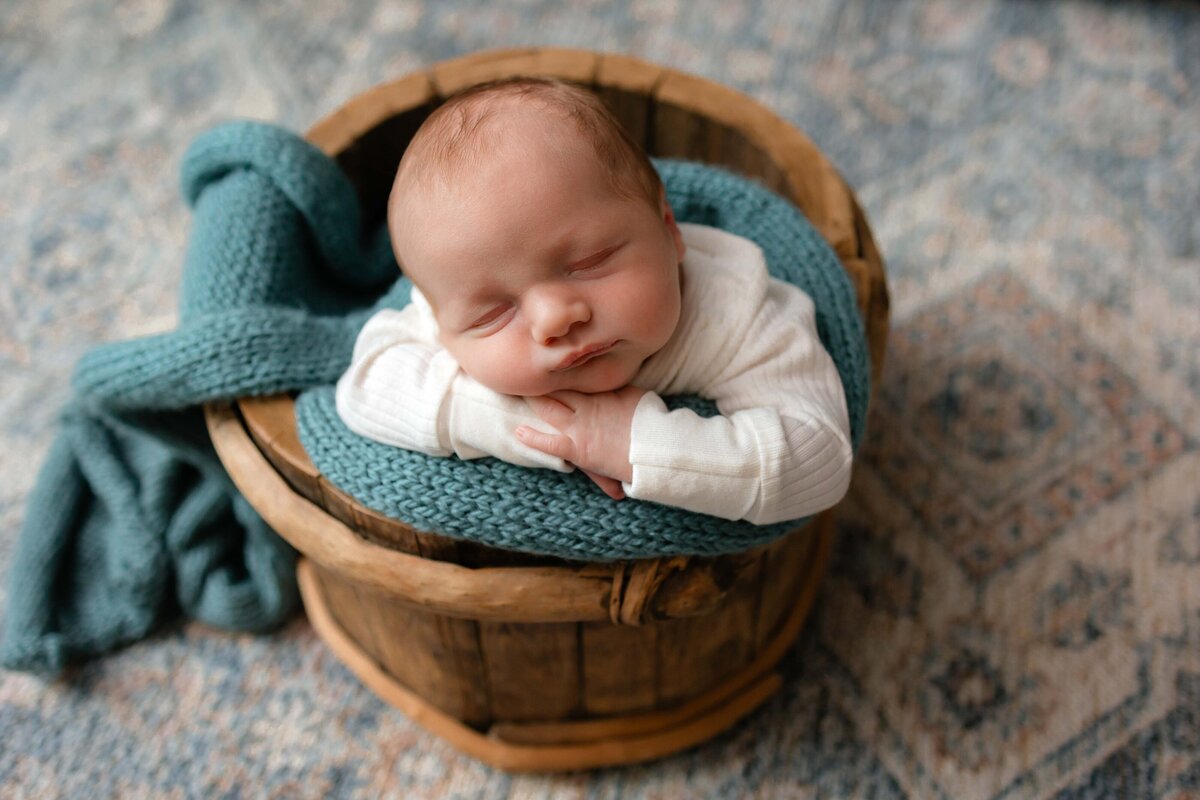 Lifestyle newborn session in Savannah, Ga of a little boy in a bucket wearing a cute white outfit