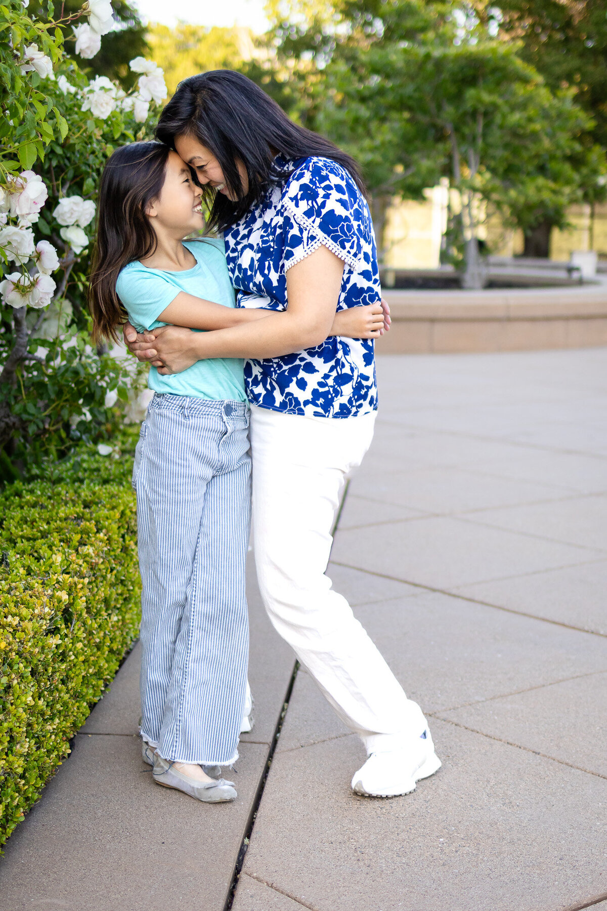 Mother and daughter laughing with their foreheads touching beside blooming white roses – Bay Area Family Portfolio - Ellobelle Photographyye