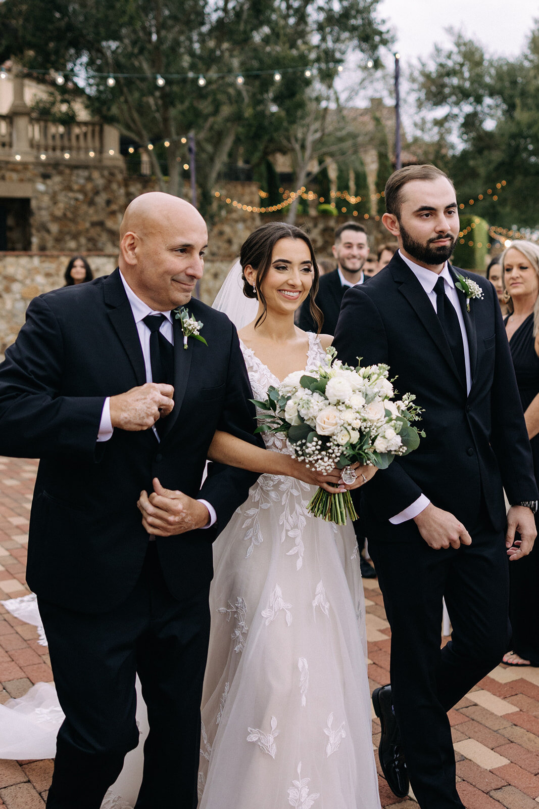 bride walking down aisle with father and brother at bella collina wedding photos​