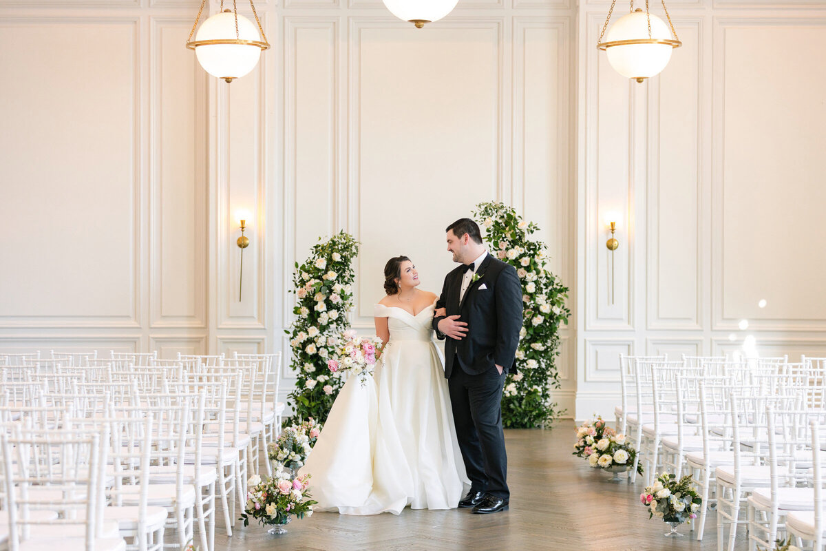 portrait of the couple walking down the aisle with a floral arch behind them in the Governor’s Room at The Adolphus in Dallas, capturing a timeless and elegant wedding moment.