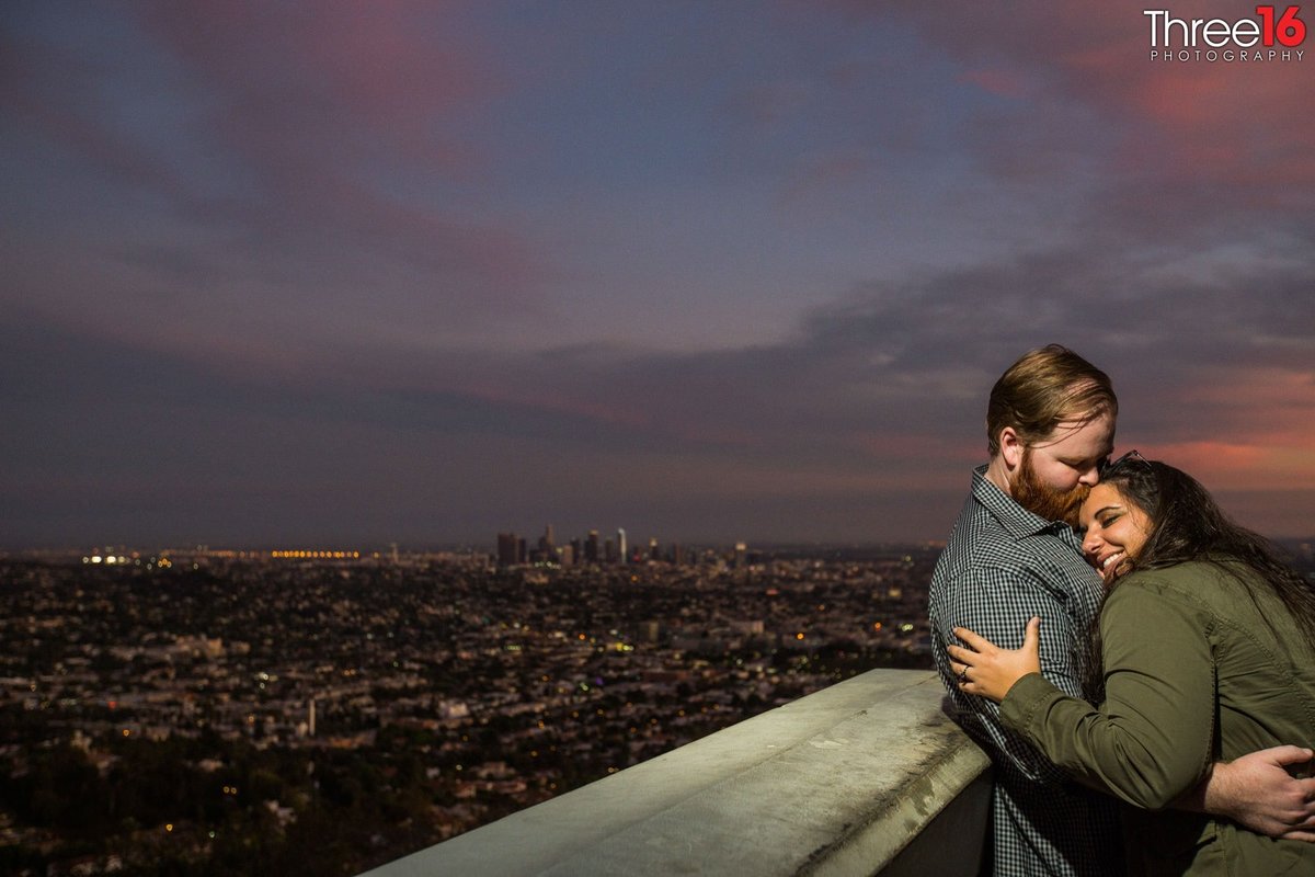 Engaged couple embrace each other on the balcony at the Griffith Observatory during sunset