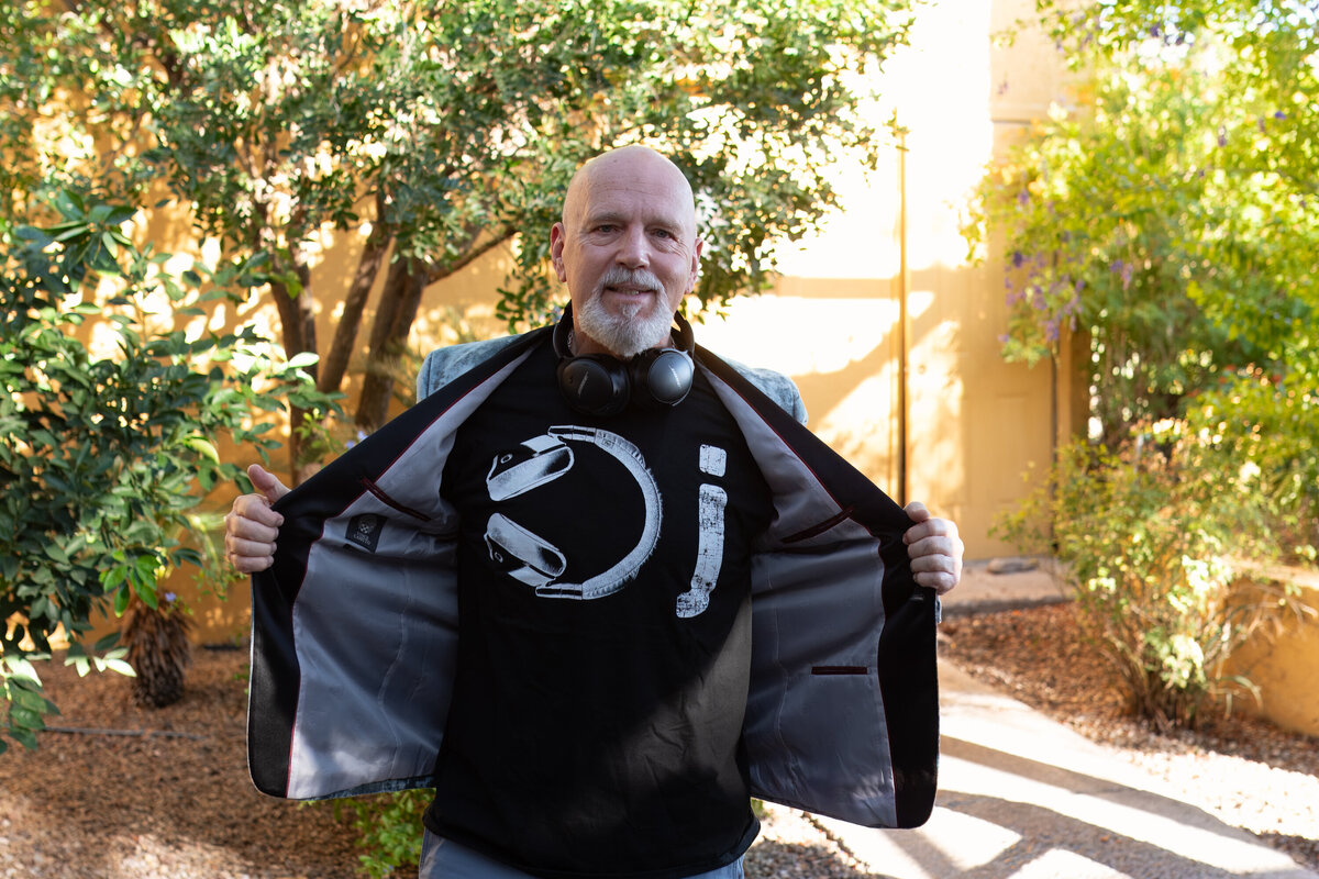 Man standing outdoors in a sunny garden area, opening his jacket to reveal a graphic T-shirt, photographed by Vyrl Photo, showcasing Tucson brand photography.