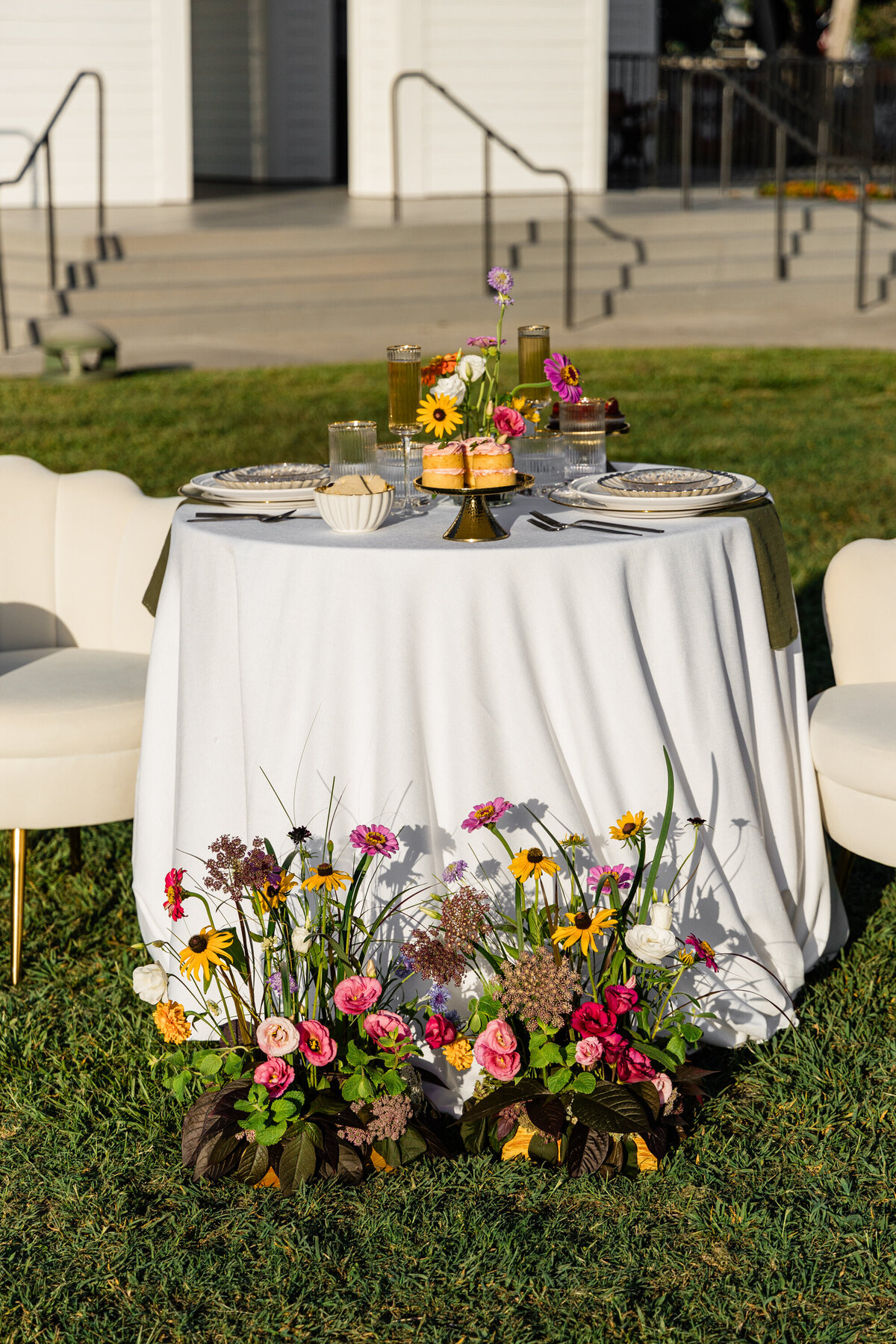 pink orange and white flowers on white table cloth with mixed metal place setting and mini chocolate cupcakes and beige shell designed chairs