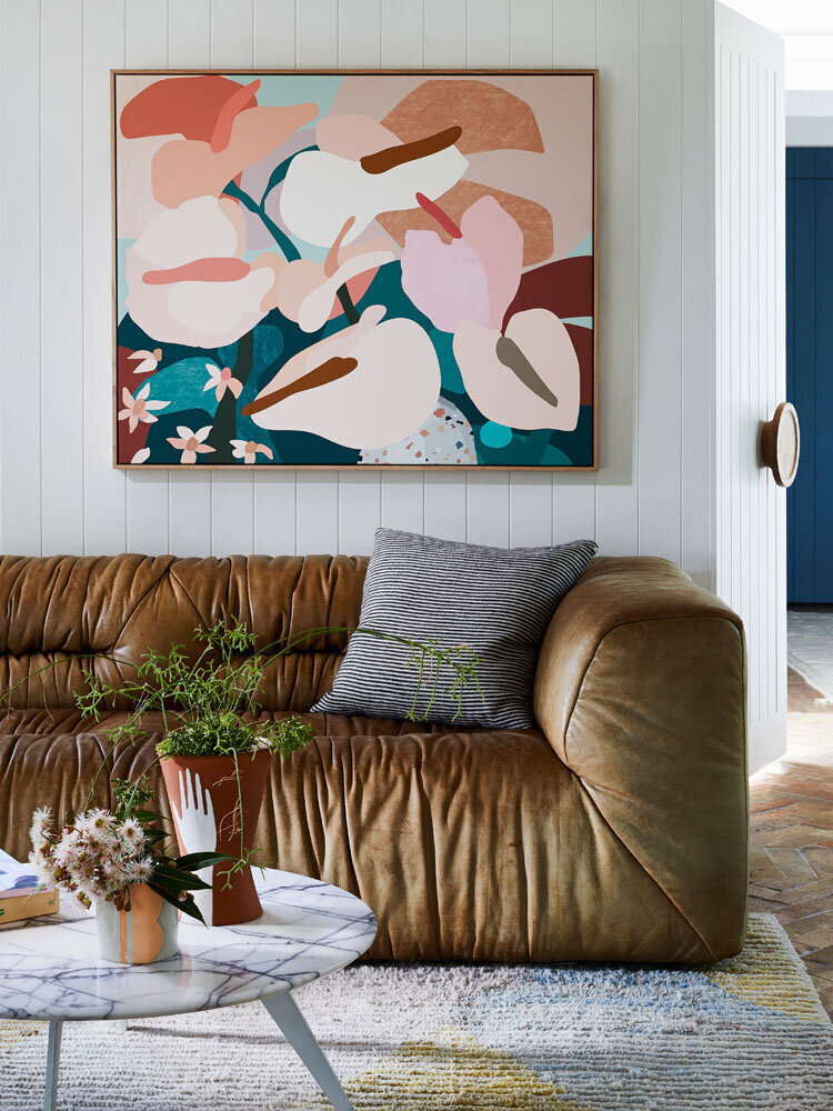 Colourful modern art above leather sofa in relaxed Melbourne living room with round coffee table and greenery.
