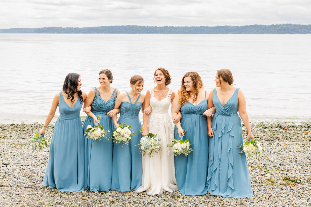 Bride-and-bridesmaids-enjoy-photo-time-on-beach-at-Lincoln-Park-in-West-Seattle-Photo-by-Joanna-Monger-Photography