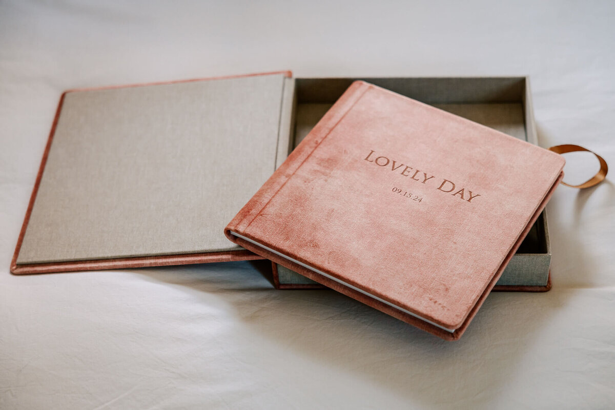 Light pink velvet album of family photos, resting on top of its matching pink velvet storage box with grey linen lining and a bronze ribbon pull.