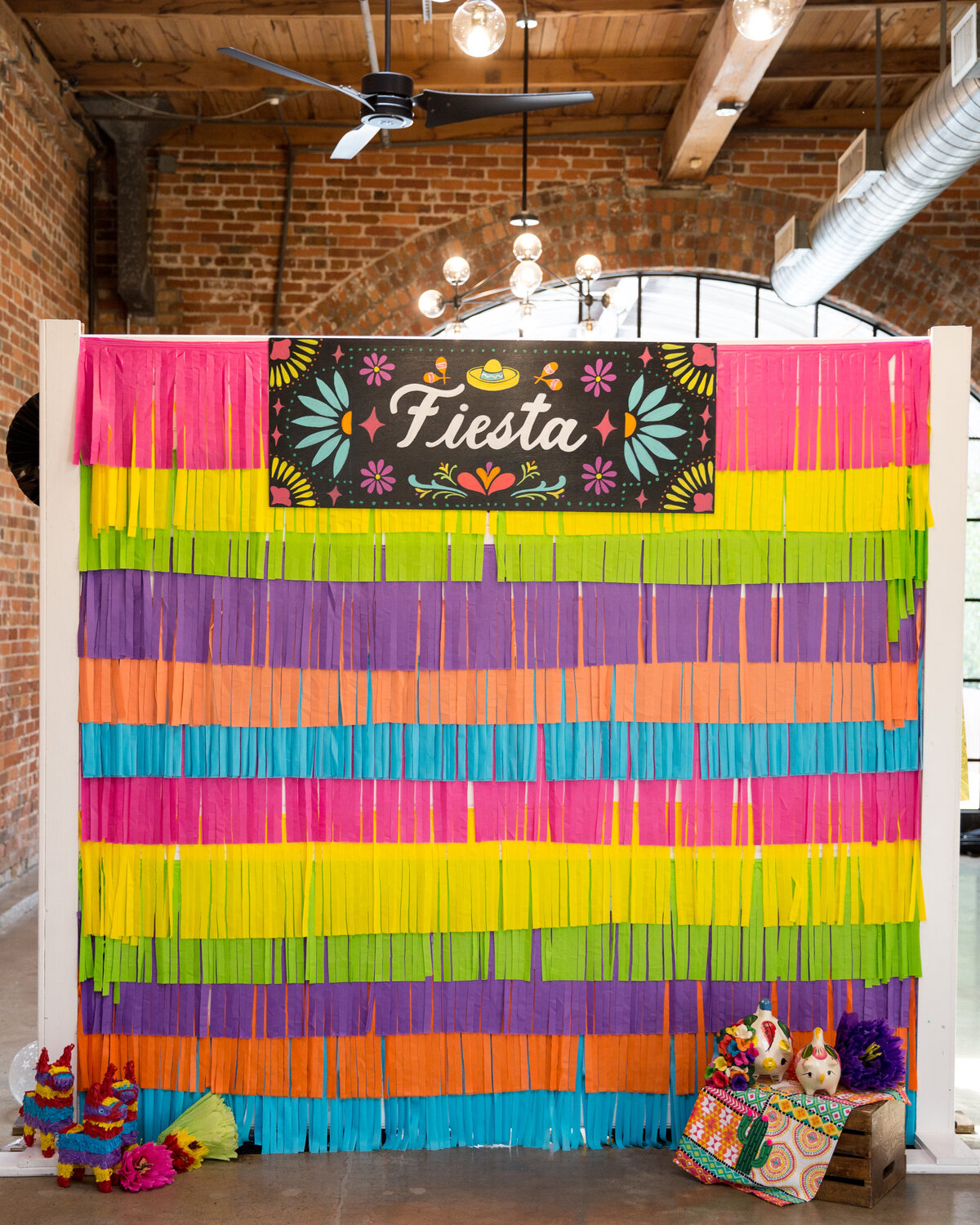 Colorful fiesta themed party backdrop decorated with streamers and small pinatas