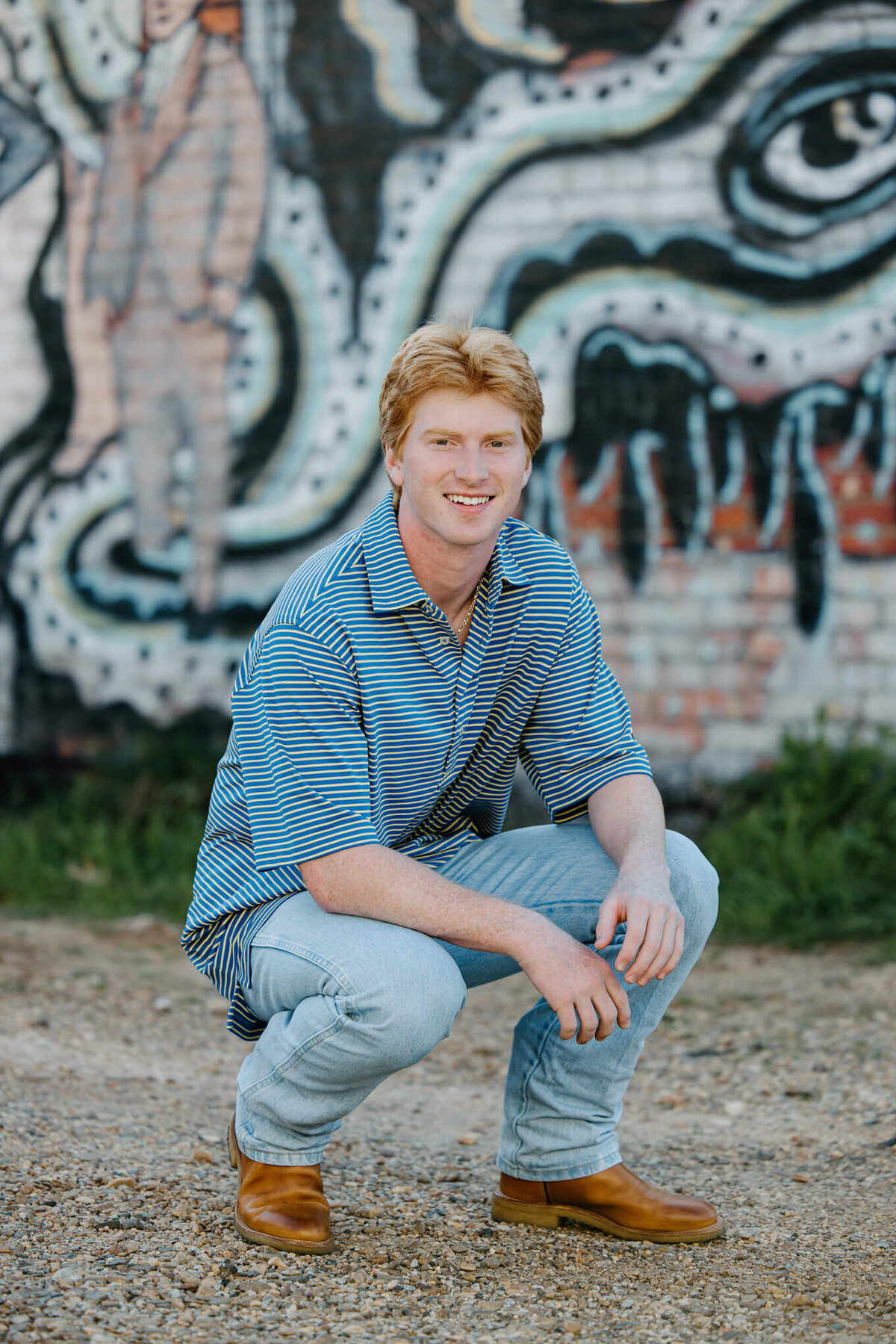 boy senior squatting in front of painted mural wall in the Longview, TX art district