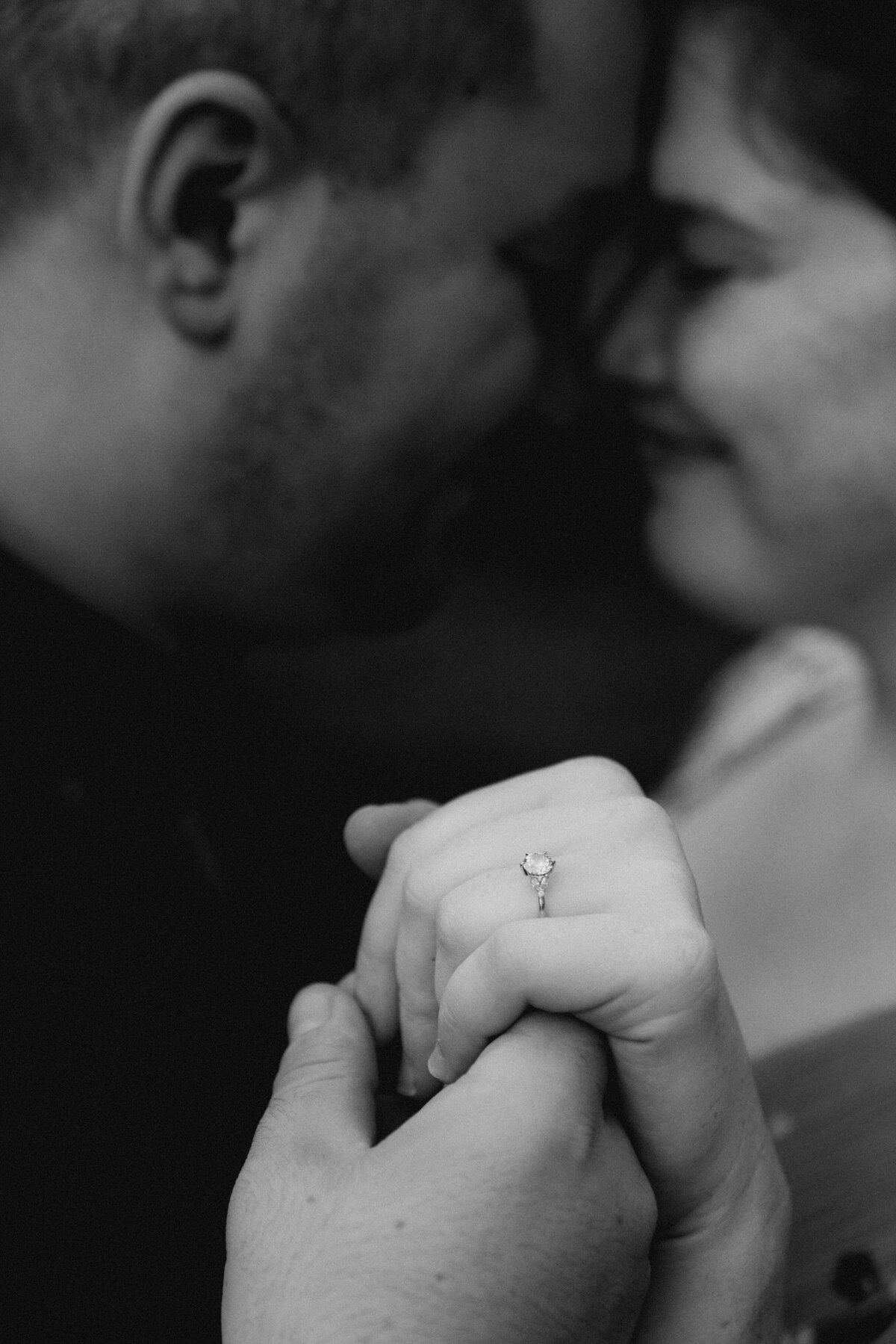 A couple leans in close, the engagement ring is in focus.