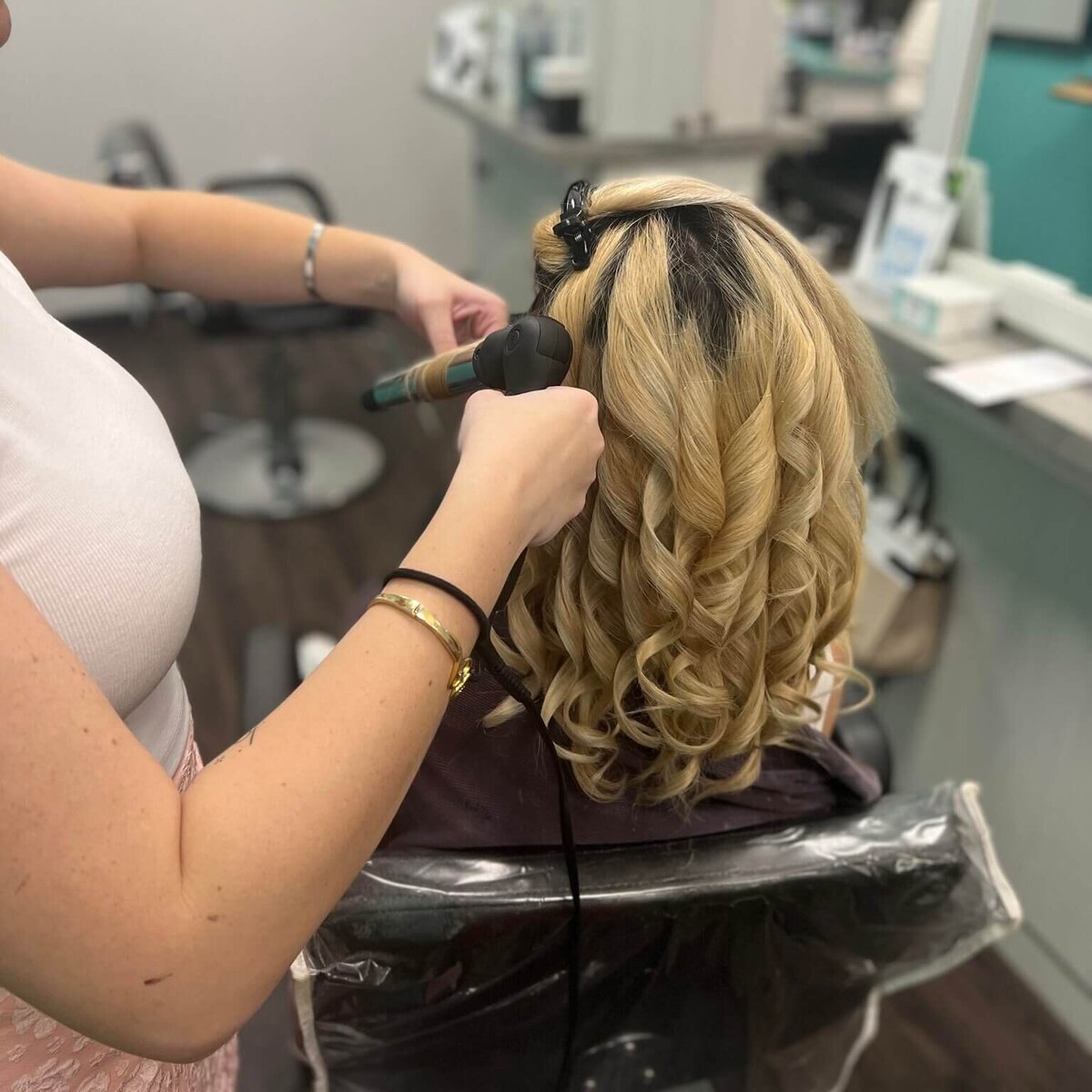 A hairstylist curling a client's blonde hair, showcasing the intricate hairstyling process at 212 Salon, Spa, & Barbershop.