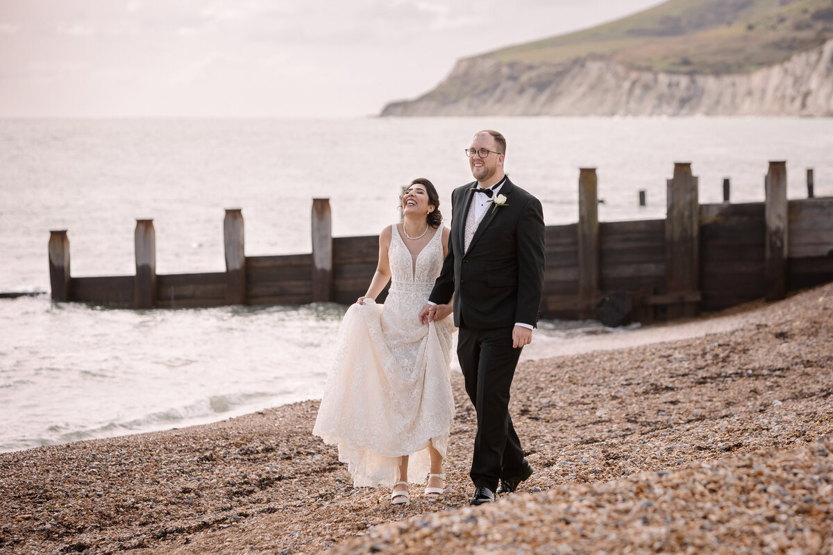 A bride and groom walking on a pebbled beach