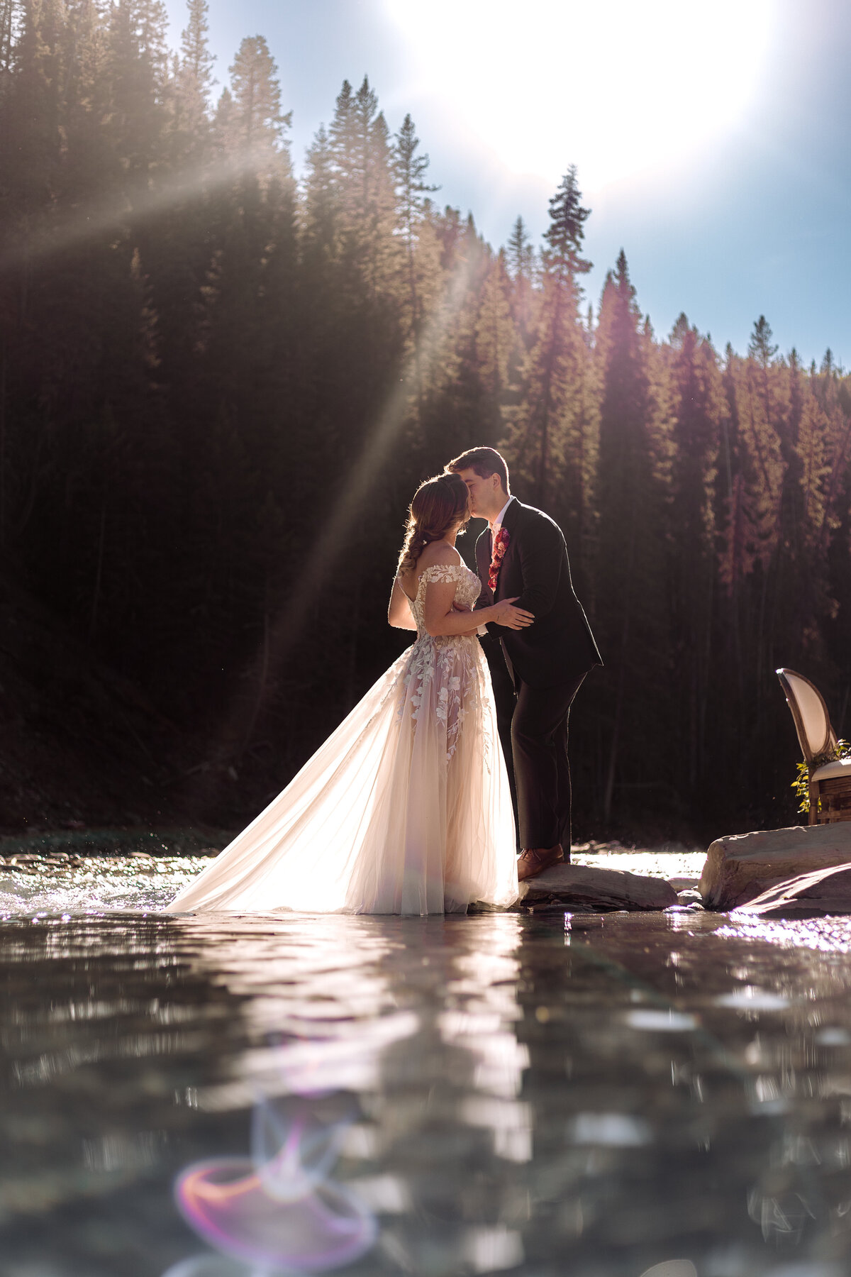 Bride and groom kissing in the water with a sunflare behind them