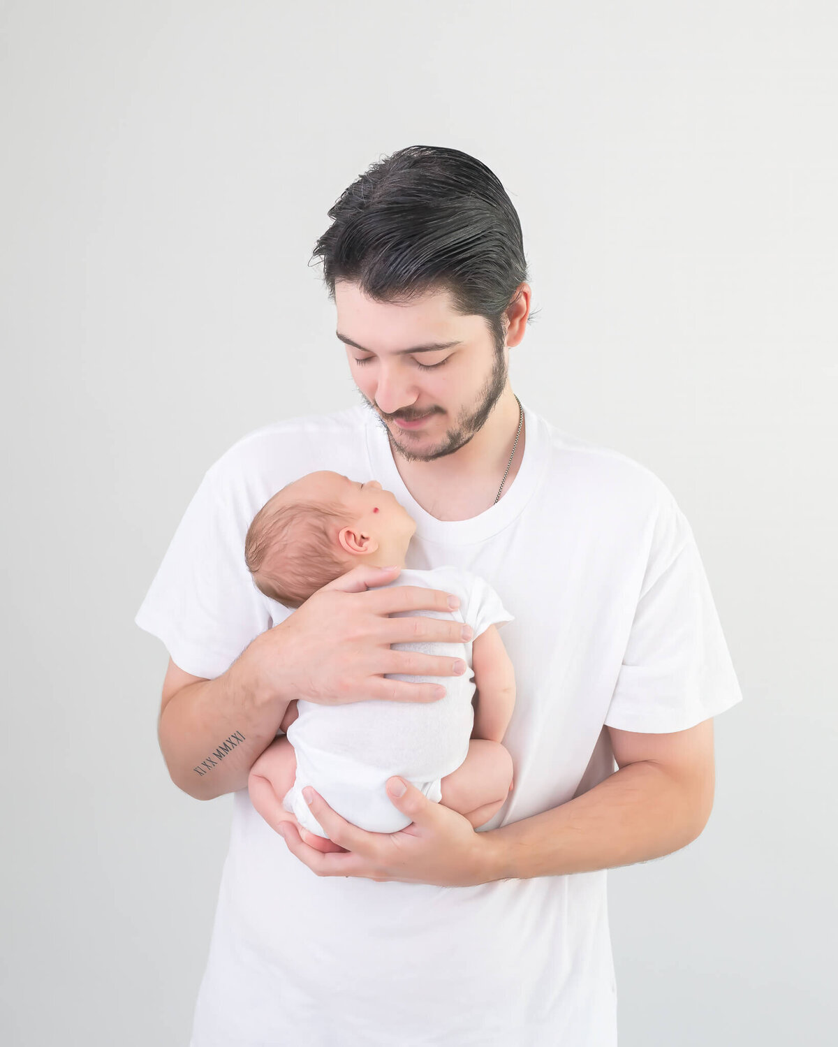 beautiful timeless studio portrait of dad with newborn, both wearing white on white backdrop