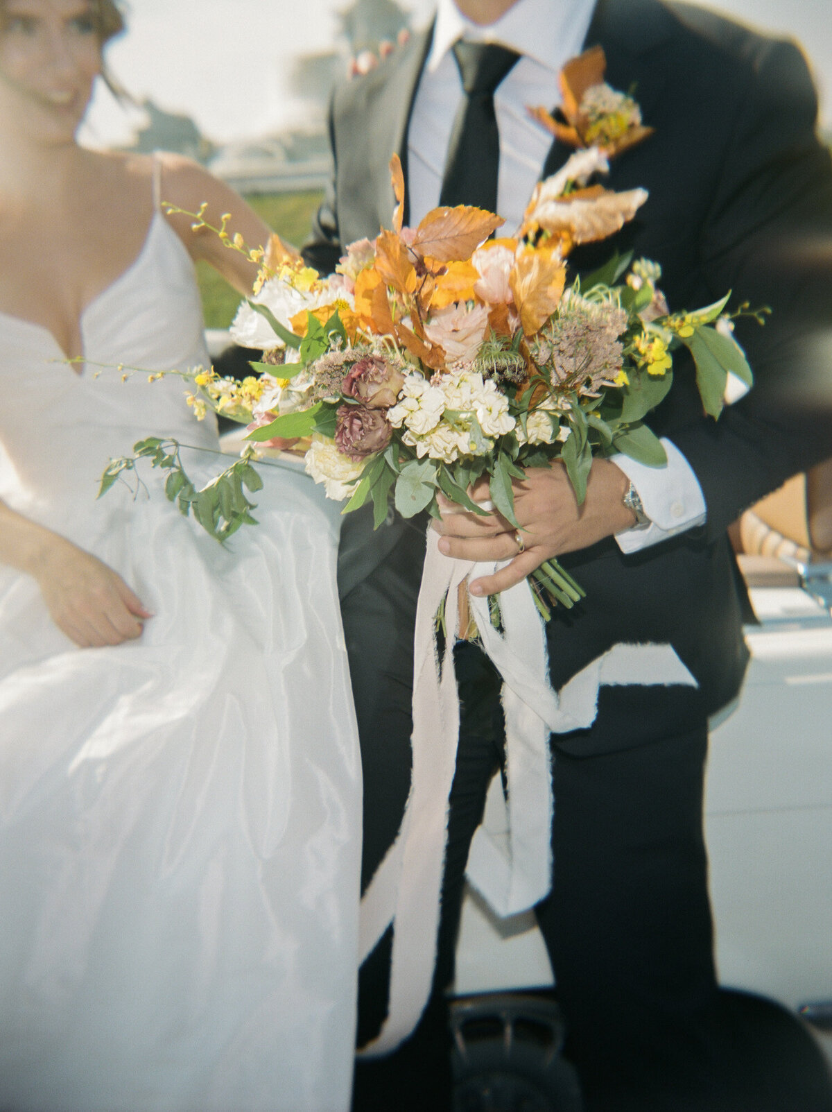 A groom helps his bride with fall bridal bouquet in Detroit, Michigan