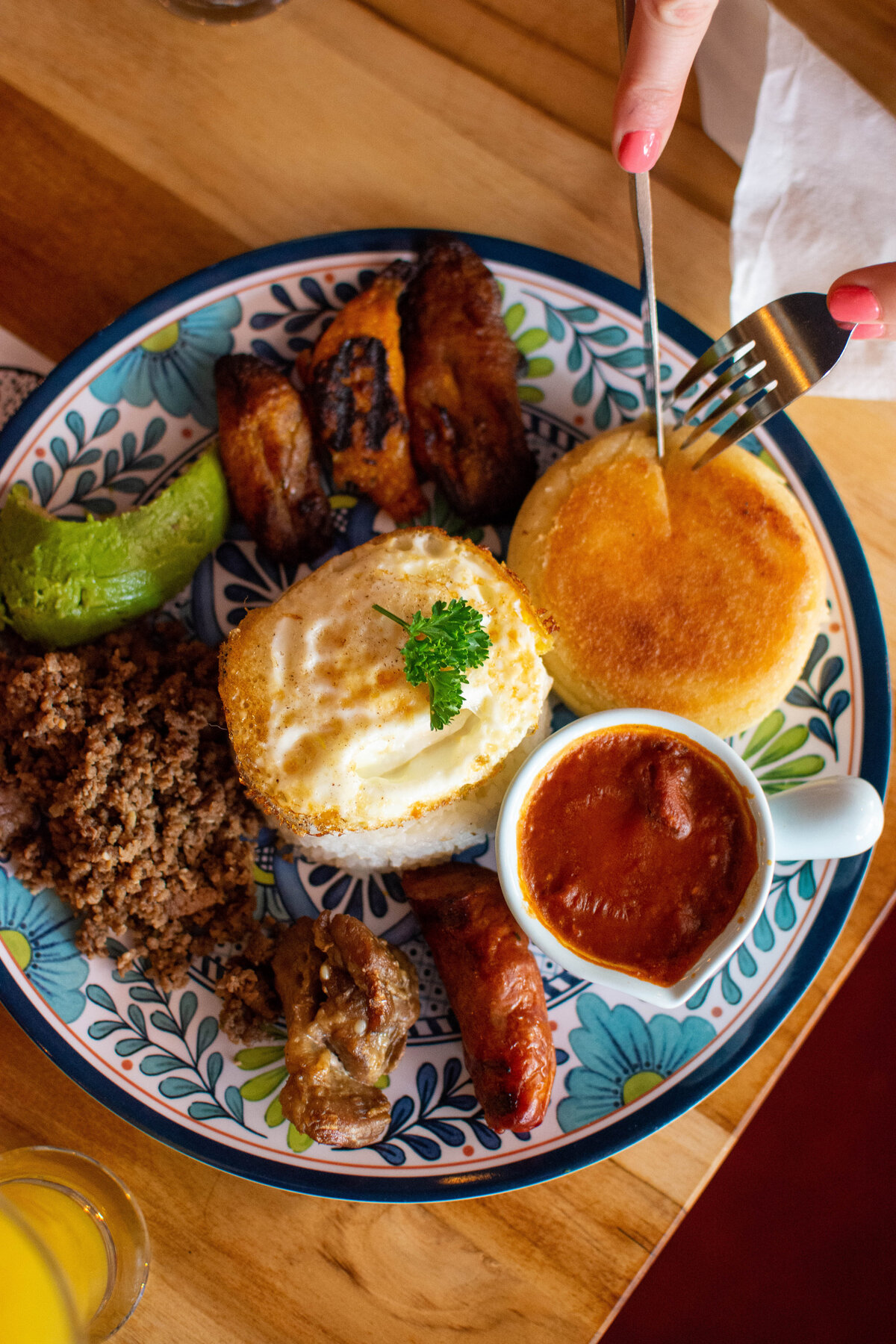 Hands with fork and knife reaching over blue and white plate filled with traditional Colombian food