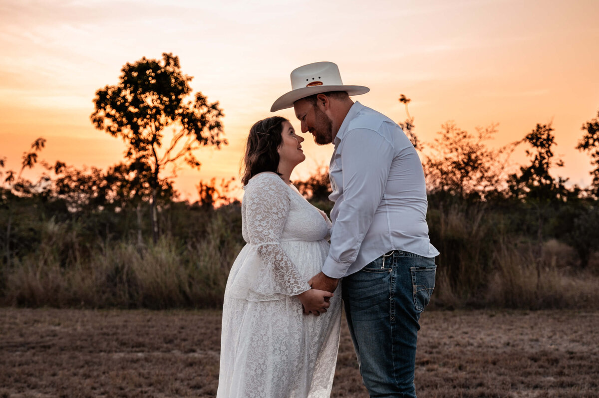 pregnant woman and partner holding each other in a paddock at sunset - Townsville Maternity Photography by Jamie Simmons