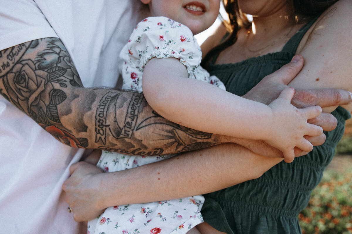 Father, mother and infant hug each other close as arms is the focus of their photo. 
