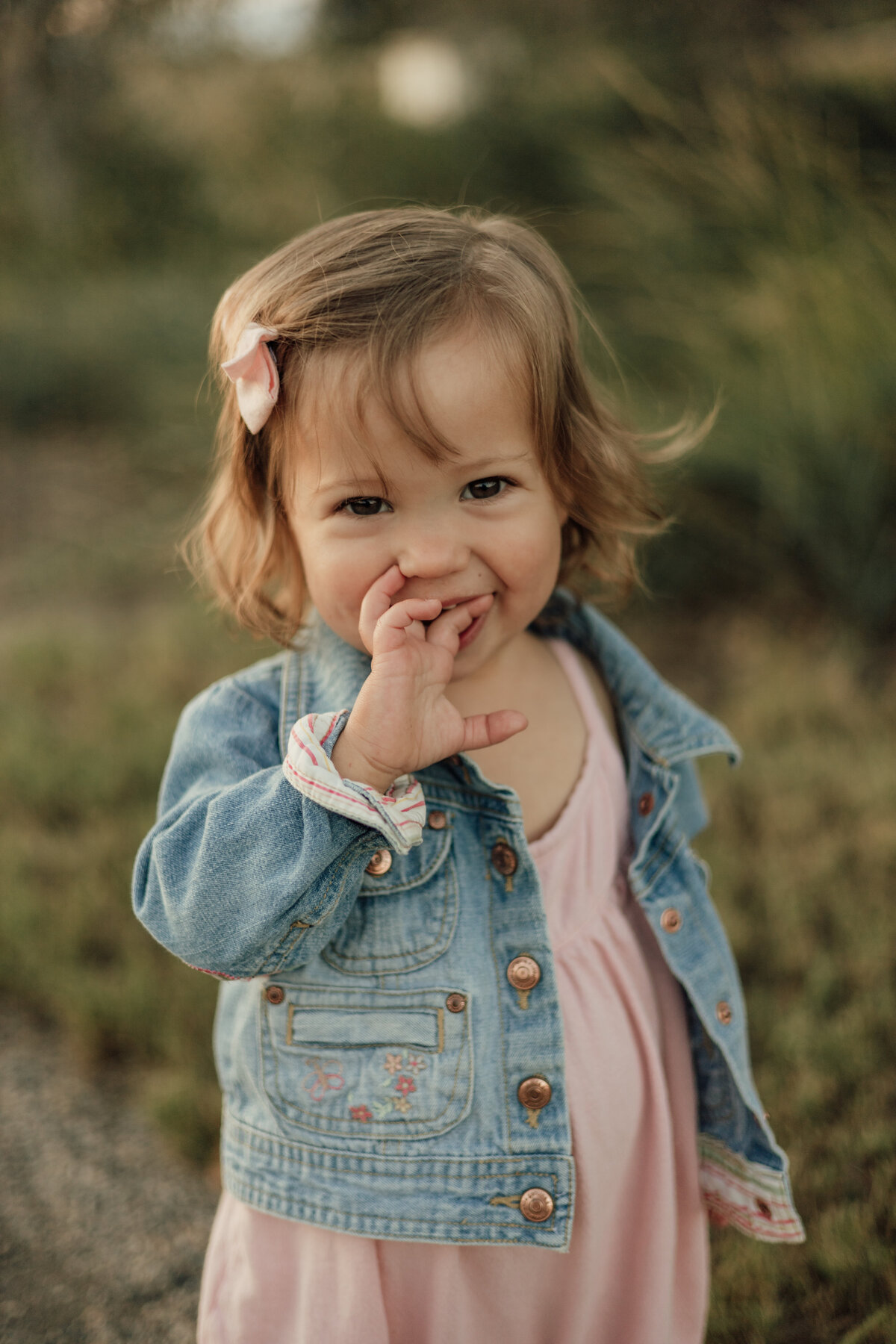 little girl smiling with fingers in her mouth looking at the camera during family session in longmont colorado with alexis adkins photography