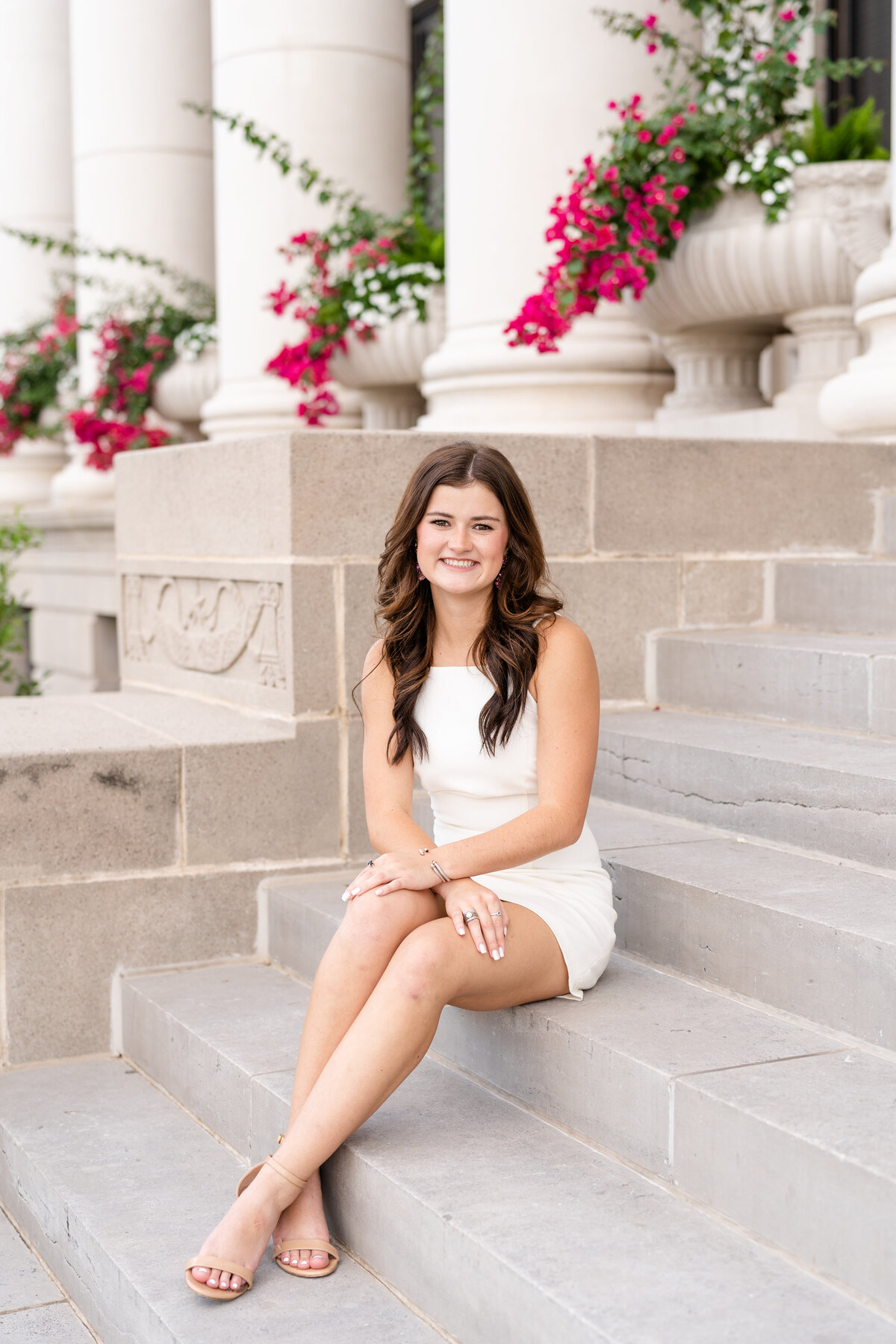 Texas A&M senior girl sitting on Administration Building stairs in white dress and smiling