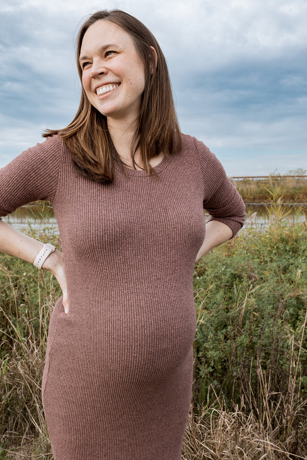 Maternity Photographer, an expectant woman smiles near the edge of a lake