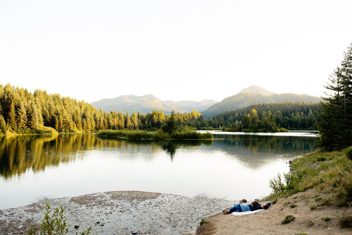 Engaged Couple lays together and enjoys the view of an alpine lake