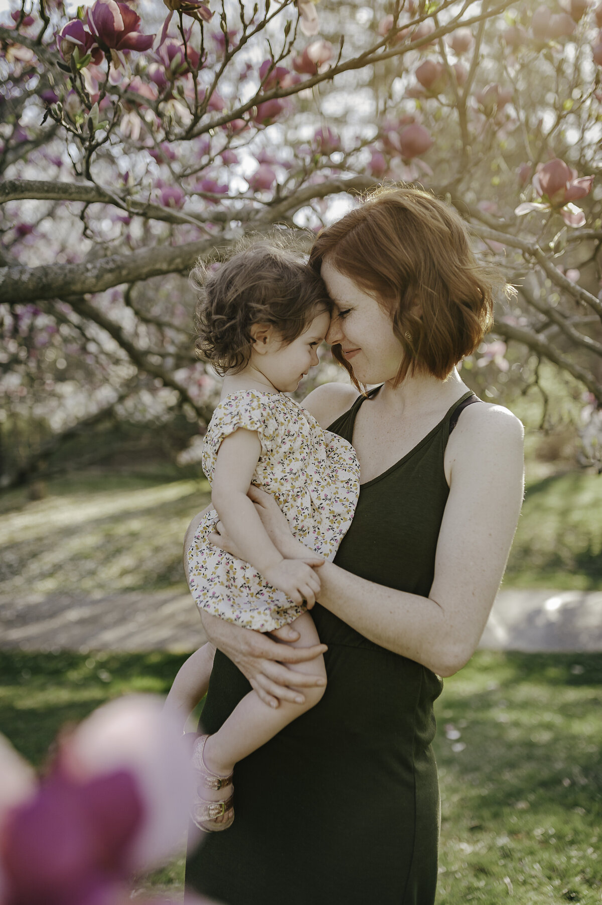 Verona B Photography captures a stunning photo of a mom and her daughter in front of the beautiful magnolia tree blossoms at the Nature Realm in Fairlawn, Ohio. The spring blossoms were in full bloom, the sun was shining gloriously, and it was a perfect family photo session near Akron.