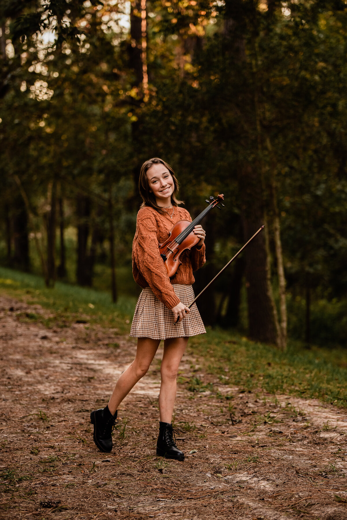 A Kingwood High School senior stands in a forest setting holding her violin.