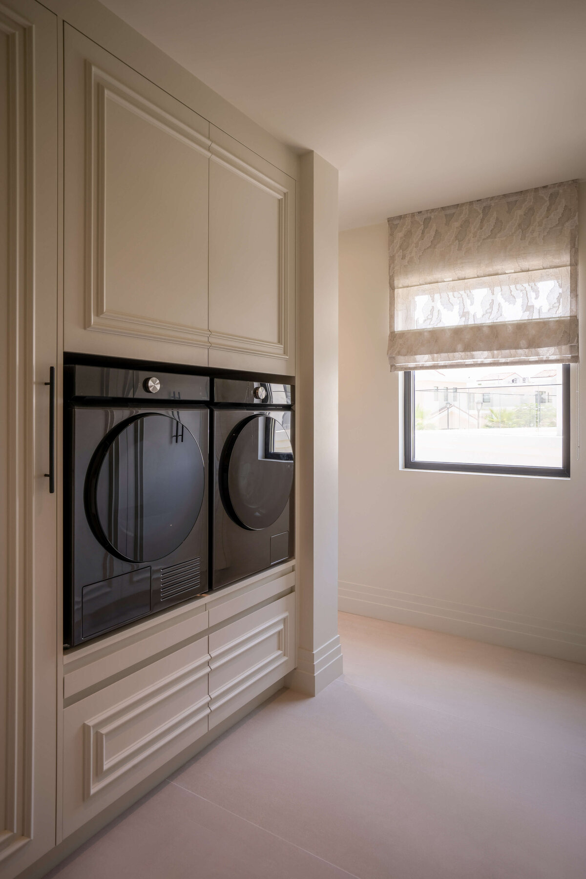 Built-in laundry and storage. The cabinets are neutral white with black hardware. The washer and dryer unit are modern and all-black.