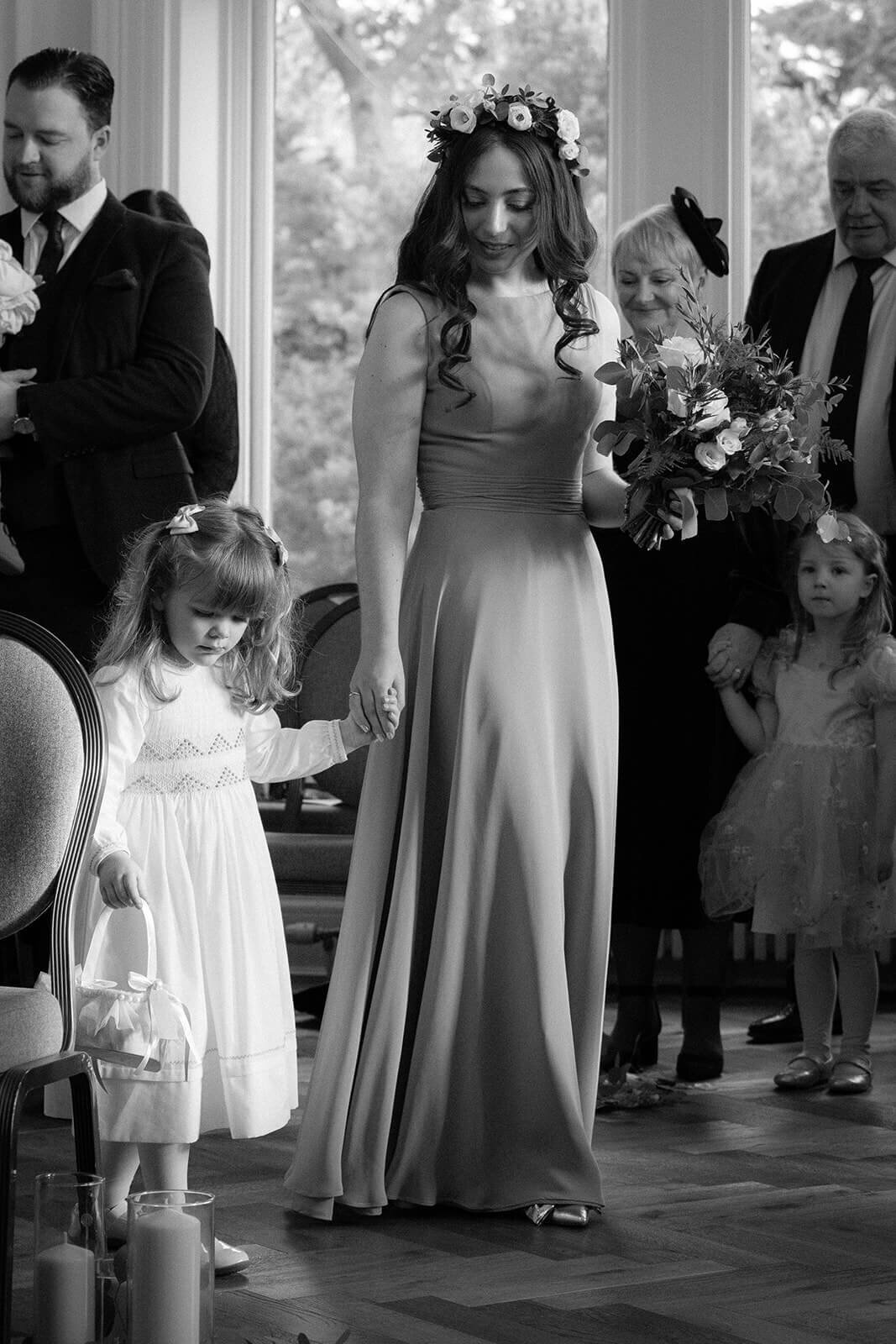 A bridesmaid and a flower girl make their way down the aisle holding hands