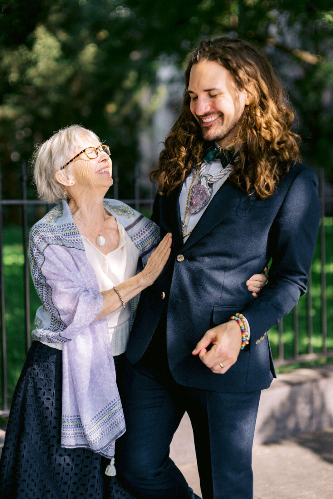 The groom is lovingly held by his mother by the waist. Trees in the background. NYC City Hall Elopement Image by Jenny Fu Studio