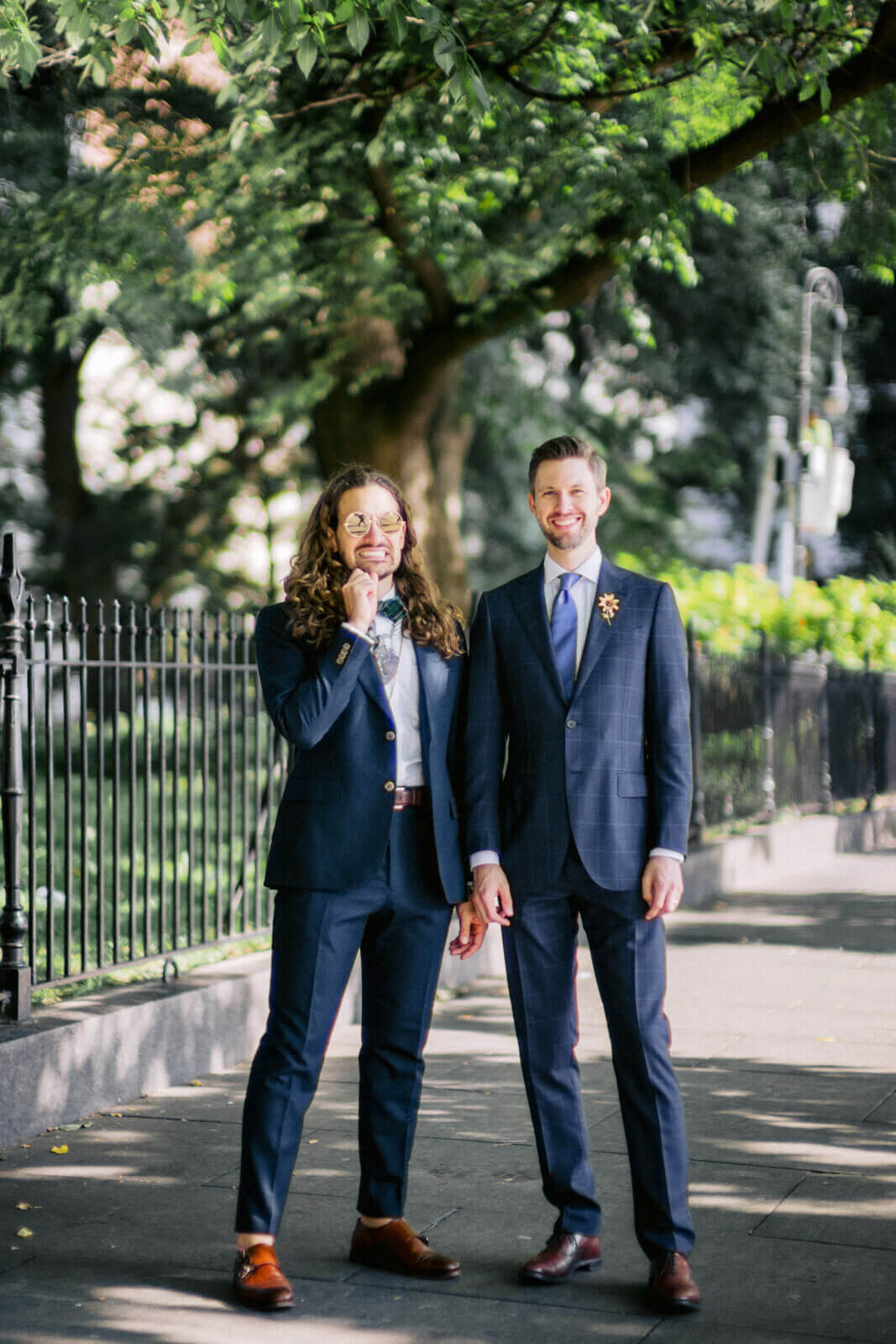 The two grooms are in a park, with trees in the background. NYC City Hall Elopement Image by Jenny Fu Studio