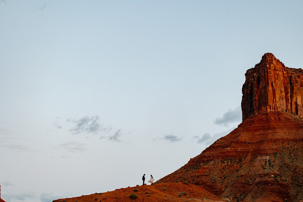 A bride and groom in the distance standing in front of some epic red rocks at Ida Gulch in Utah. 