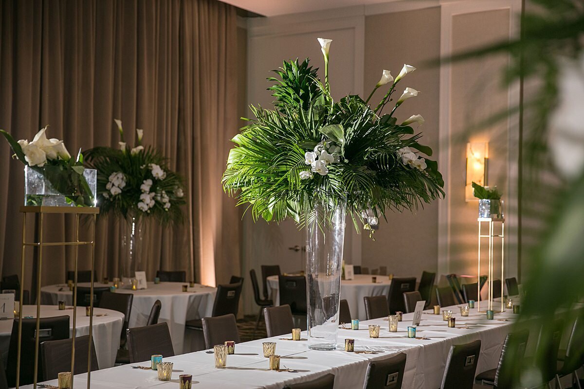 Tall tropical wedding centerpiece with palm fronds, orchids and cala lilies on long white tables with gold candles at the AC Hotel in Nashville for a sheikh wedding