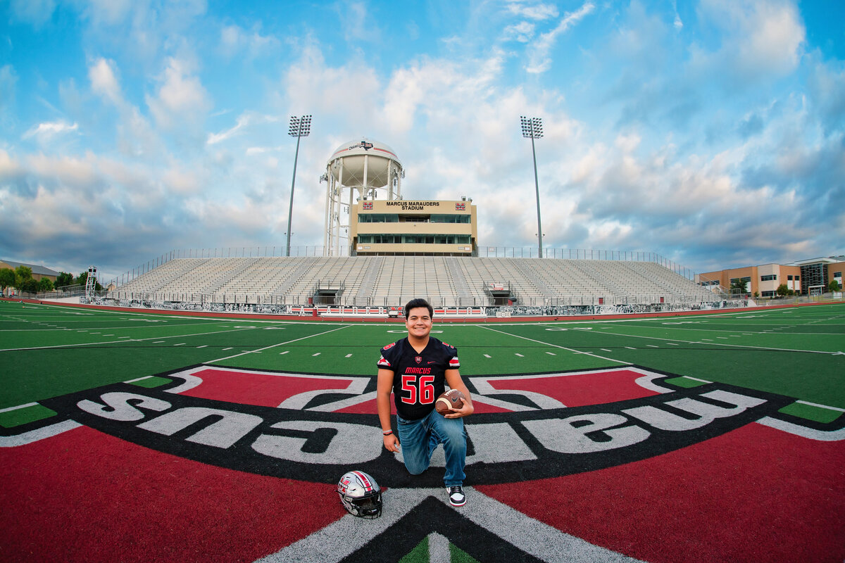 A high school senior guy poses on the football field of his high school.