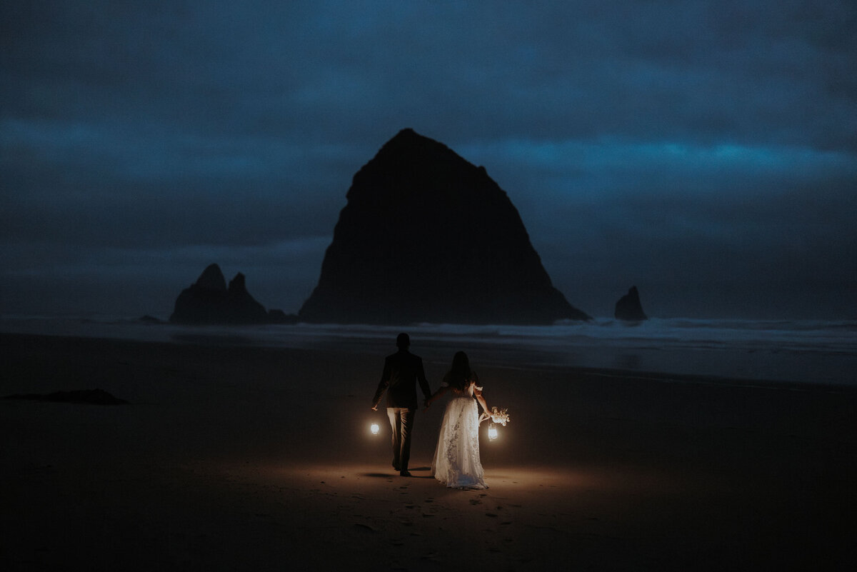 A wedding couple with lanterns walking toward Haystack Rock at Cannon Beach in Oregon.