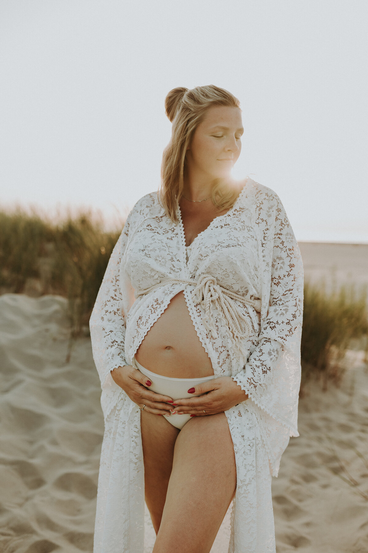 Zwangere vrouw poseert in de duinen met zonsondergang